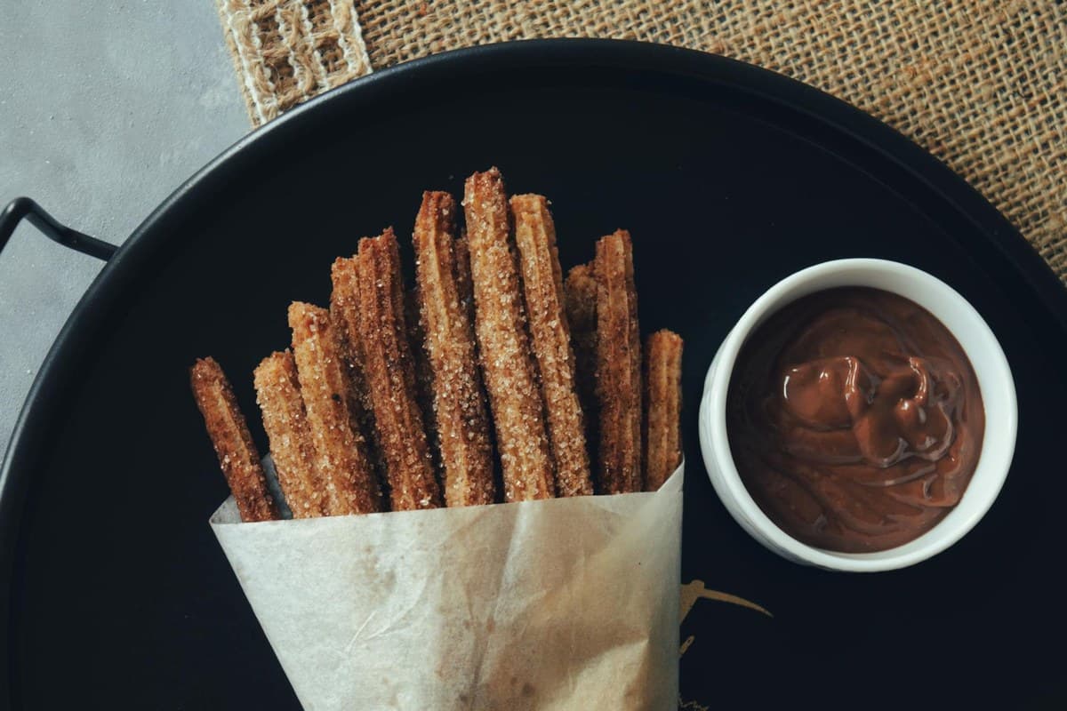 Cinnamon sugar churros with dark chocolate dipping sauce in a small bowl