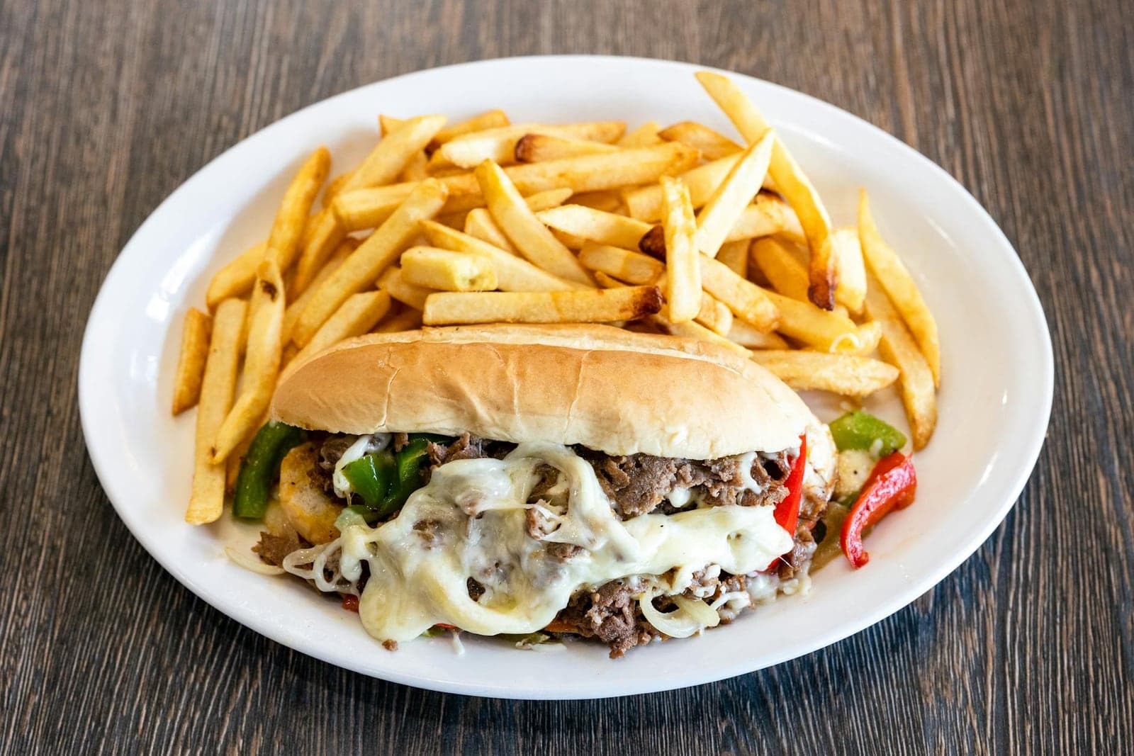 Philly cheesesteak sandwich with melted cheese, steak, peppers, and fries on the side