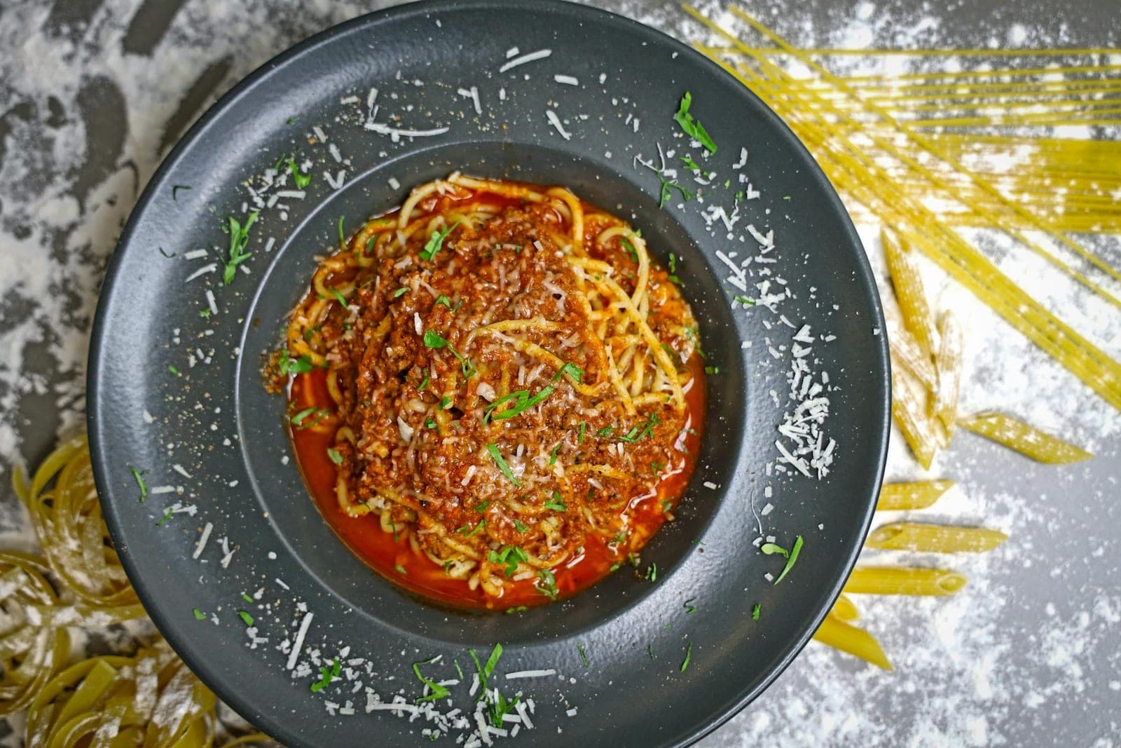 Classic spaghetti bolognese with meat sauce, parmesan, and herbs on a dark plate