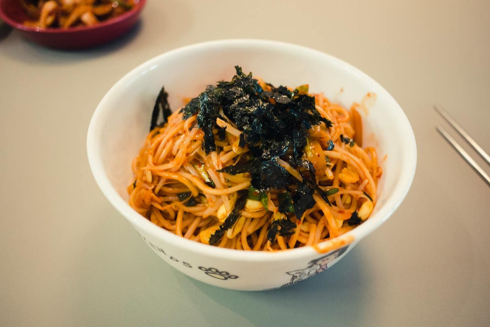 Spicy cold sesame noodles in a white bowl topped with seaweed and sesame