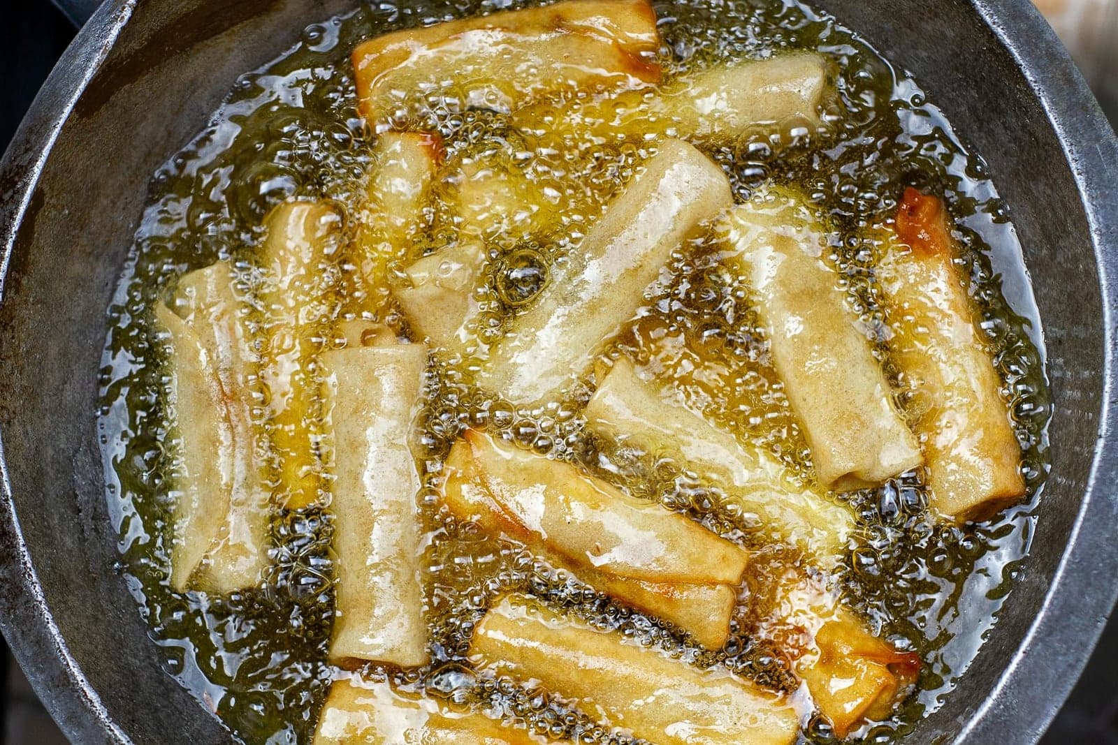 Crispy pork spring rolls frying until golden with bubbled wrappers