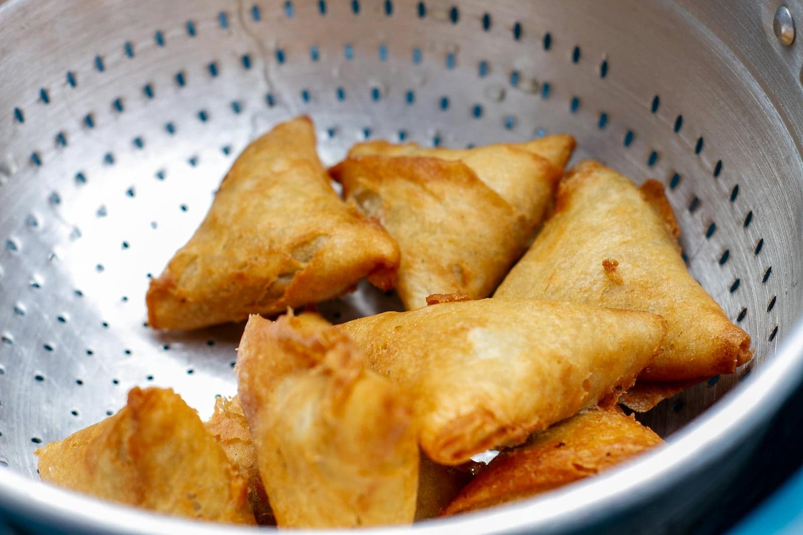 Crispy vegetable samosas cooling in a colander with golden fried pastry