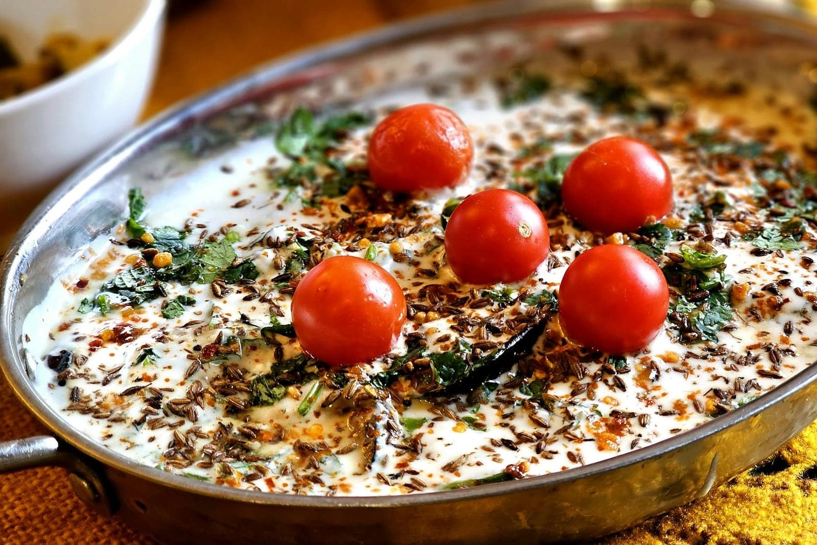 Cucumber raita in a metal dish with yogurt, spices, herbs, and cherry tomatoes
