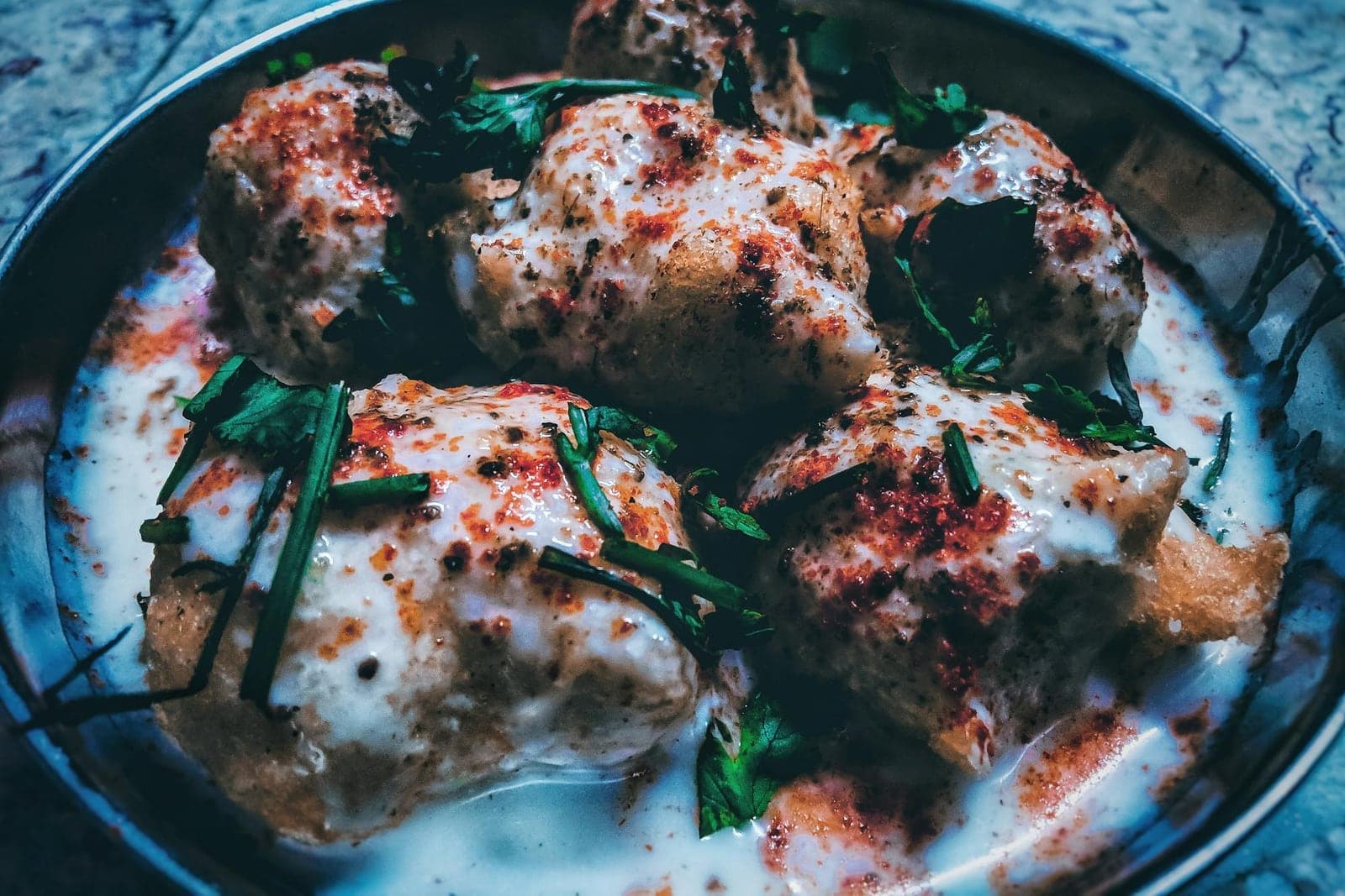 Dahi vada topped with yogurt, chutney, spices, and herbs on a blue plate