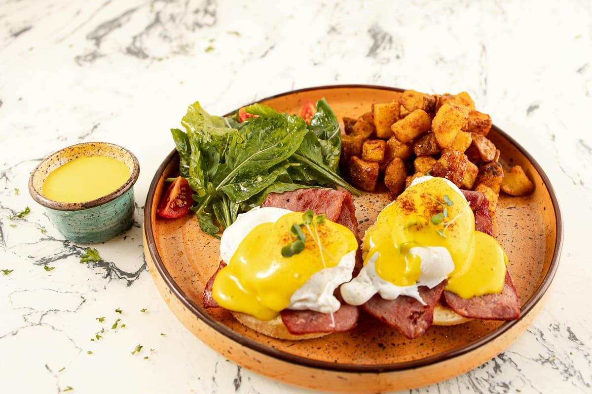 Eggs Benedict with golden hollandaise sauce, greens, and breakfast potatoes