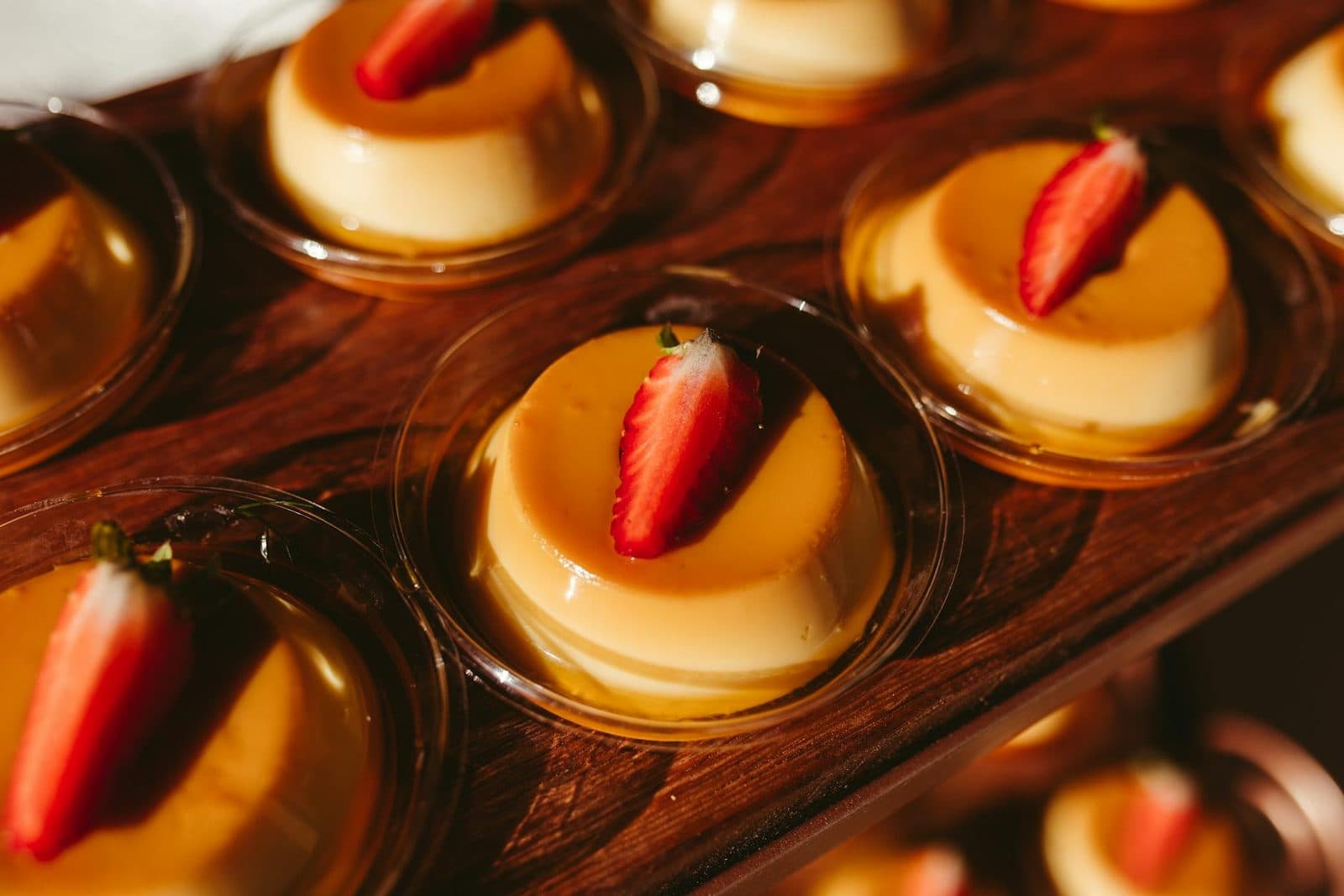 Filipino leche flan cups with caramel tops and strawberries on a wooden board