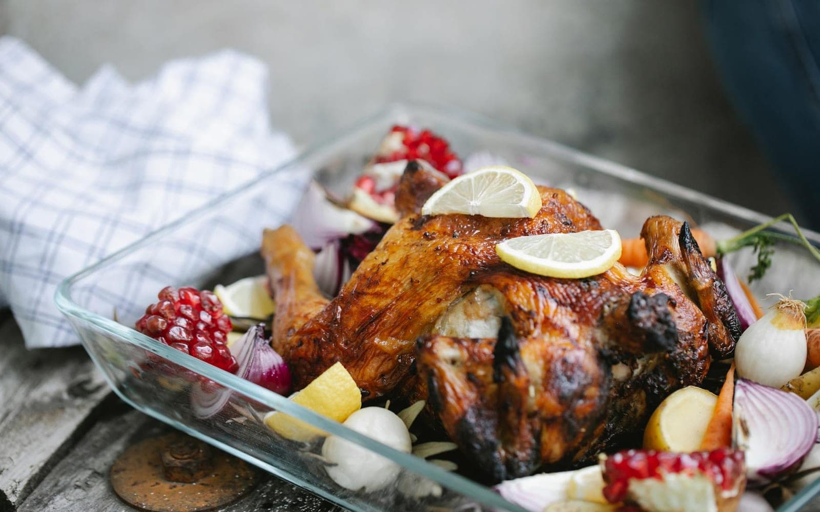 Garlic butter whole roast chicken with lemons, onions, and vegetables in a baking dish