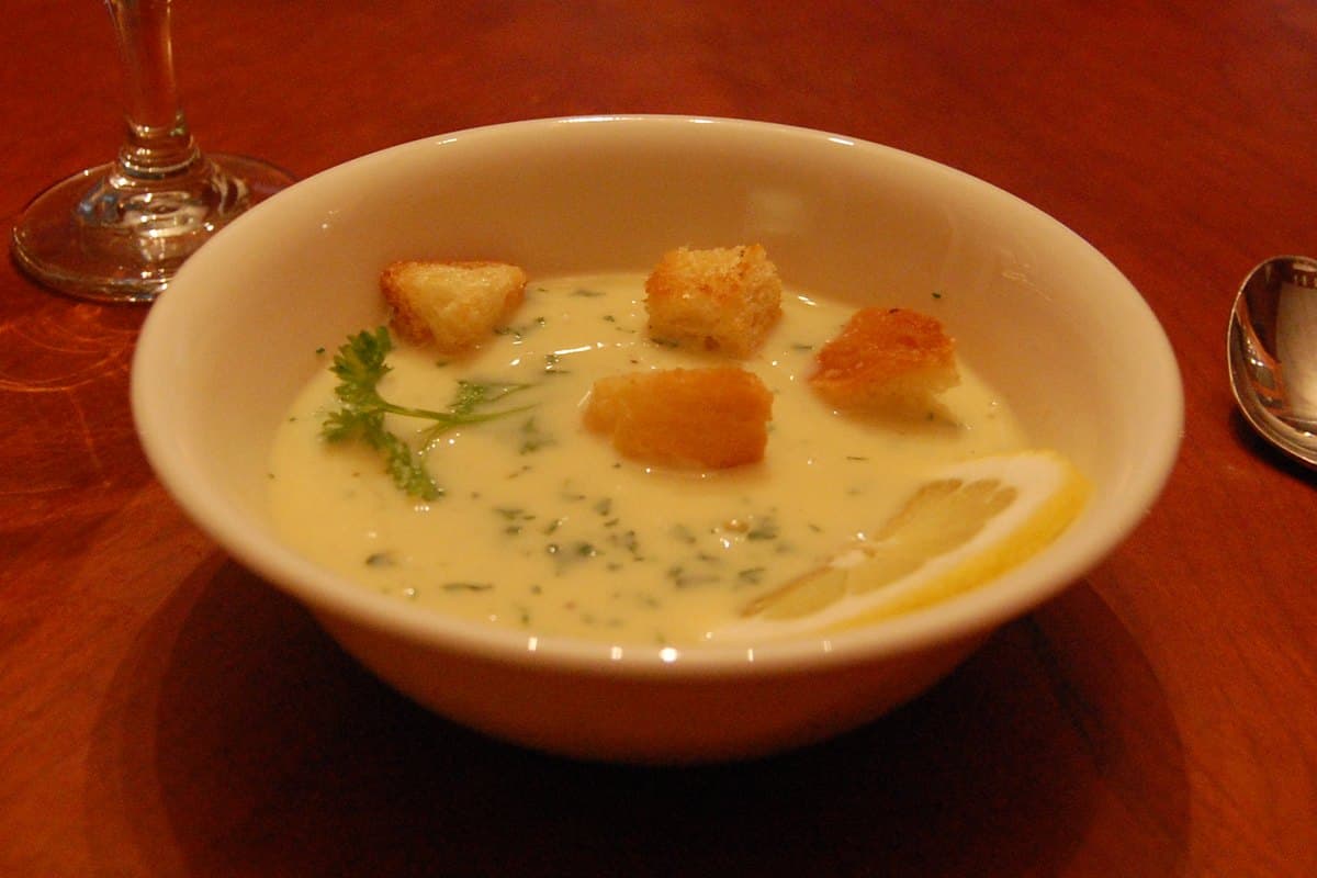 A bowl of creamy avgolemono soup with orzo and shredded chicken, garnished with fresh dill