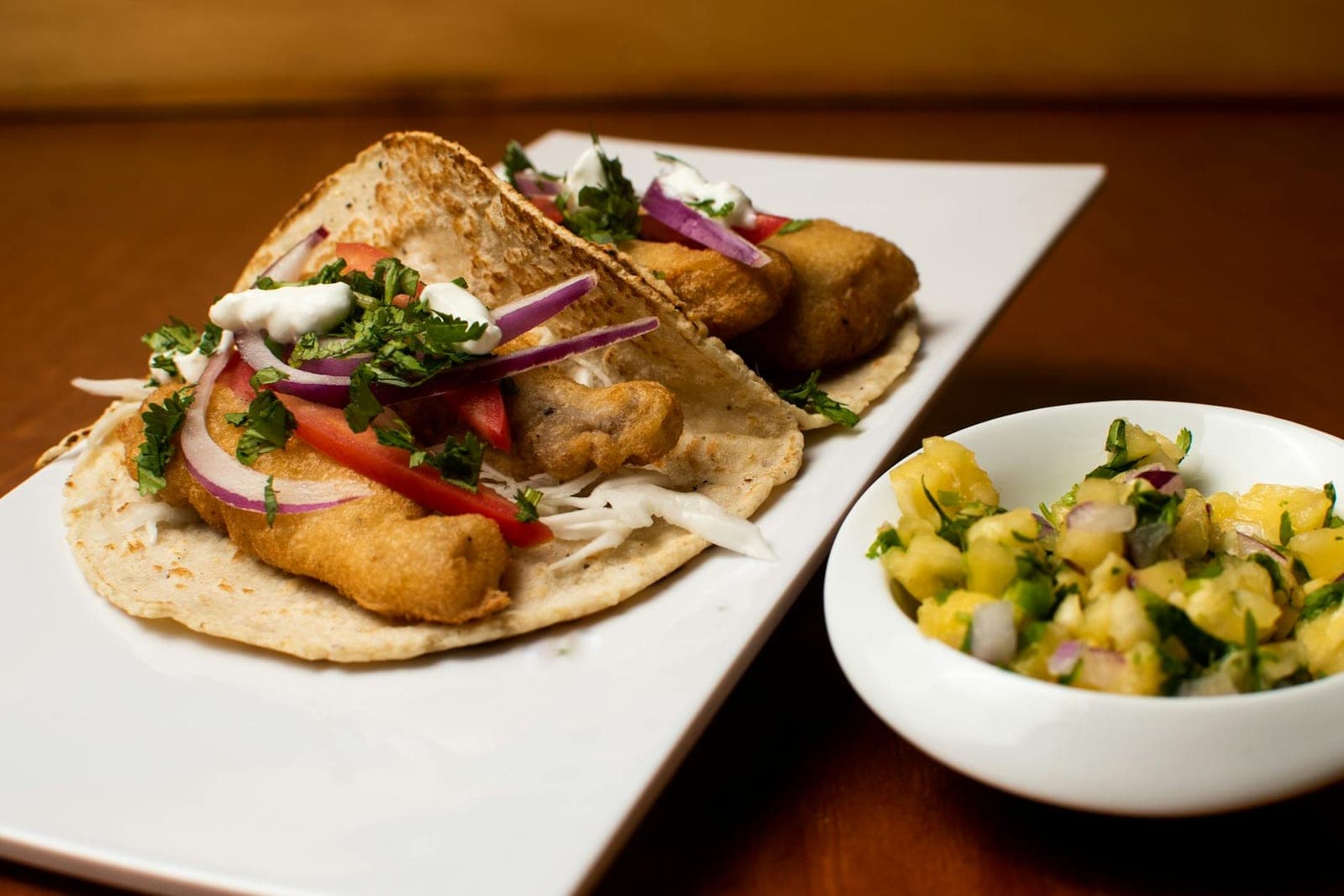 Grilled fish tacos with pineapple salsa, cilantro, onions, and fresh lime on a white plate