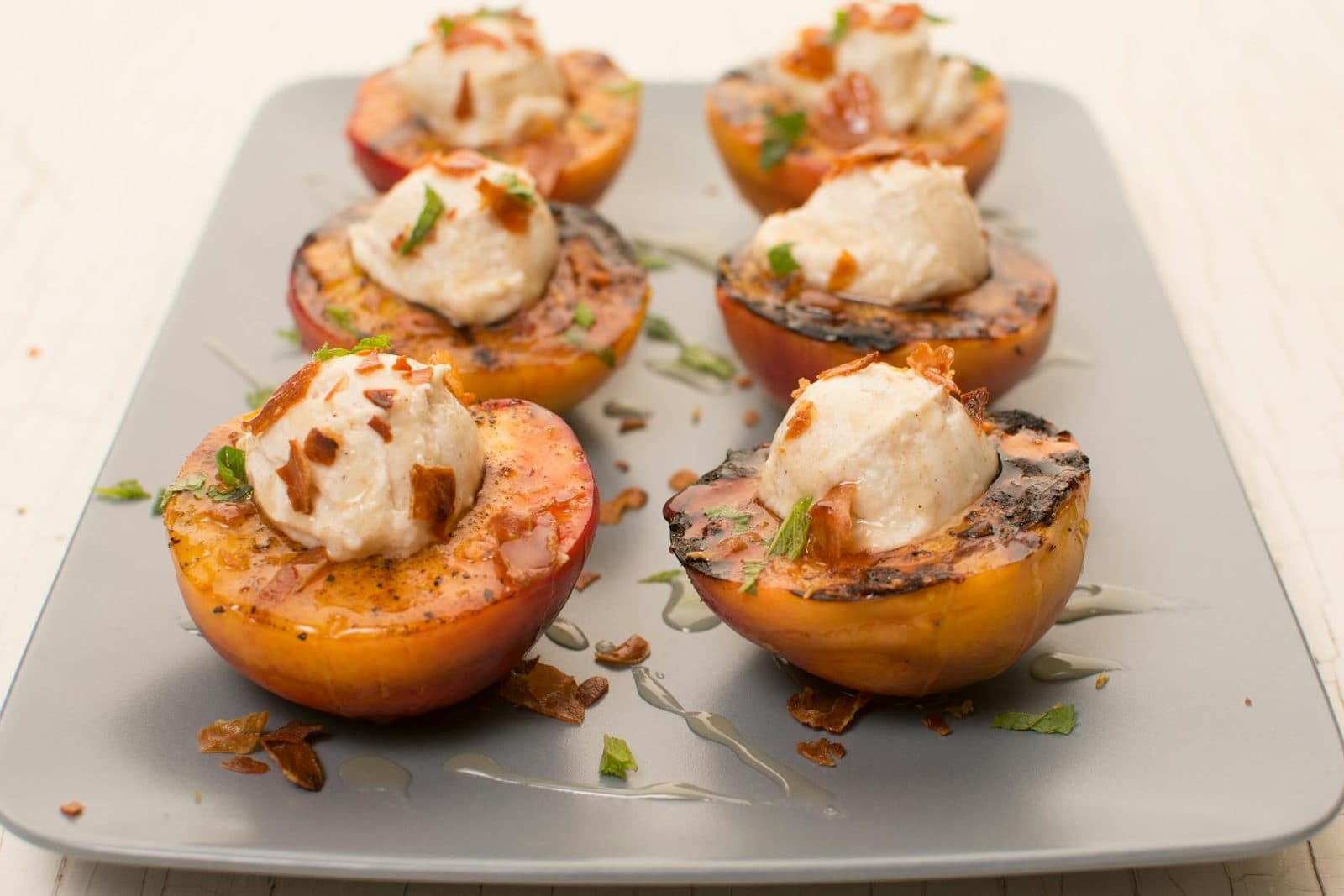 Grilled peaches with vanilla ice cream and mint on a white plate