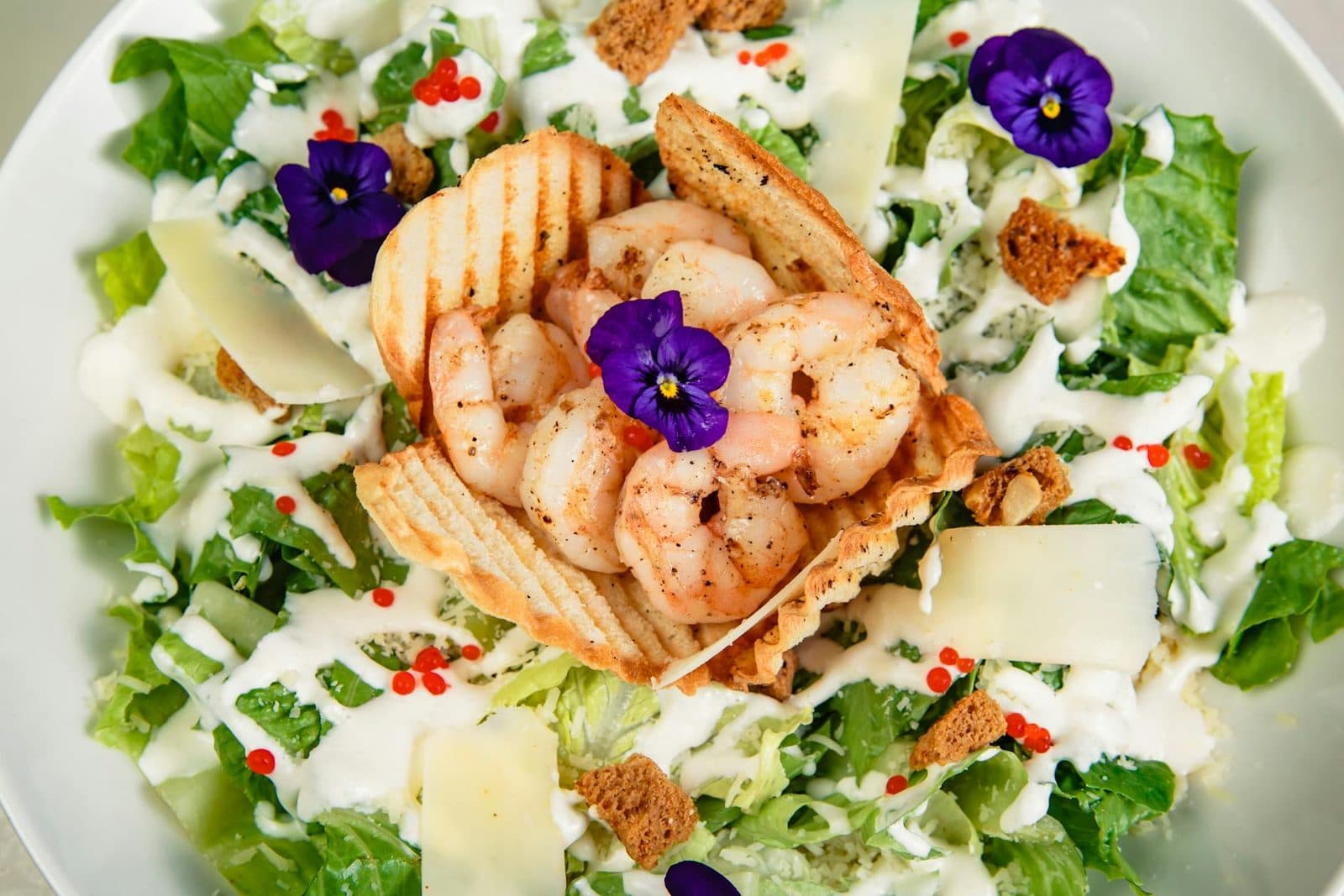 Grilled shrimp Caesar salad with creamy dressing, greens, and edible flowers