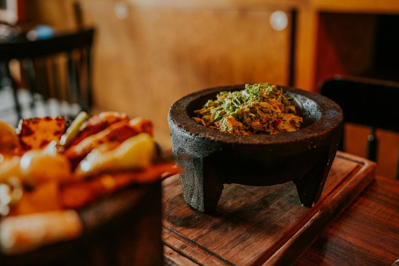 Guacamole variations in a rustic stone bowl with chips and toppings nearby