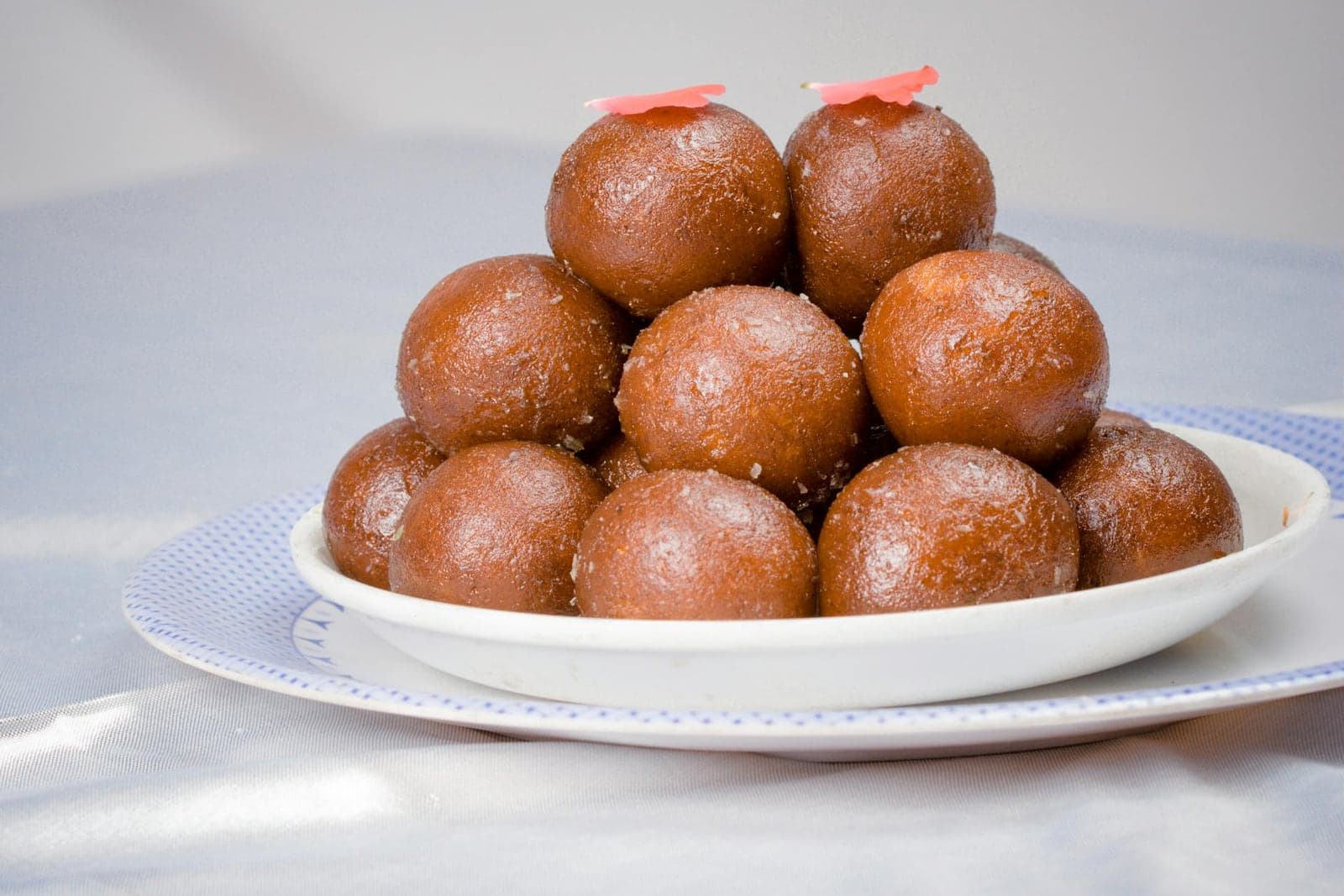 Gulab jamun arranged in a pyramid on a white plate with glossy syrup