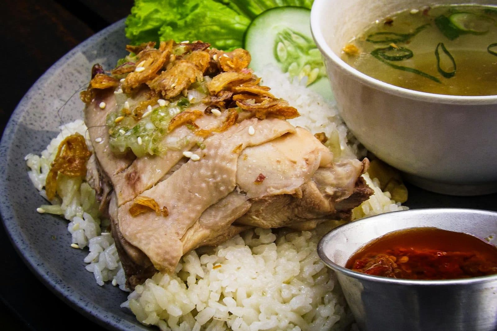 Hainanese chicken rice with sliced chicken, seasoned rice, soup, and chili sauce