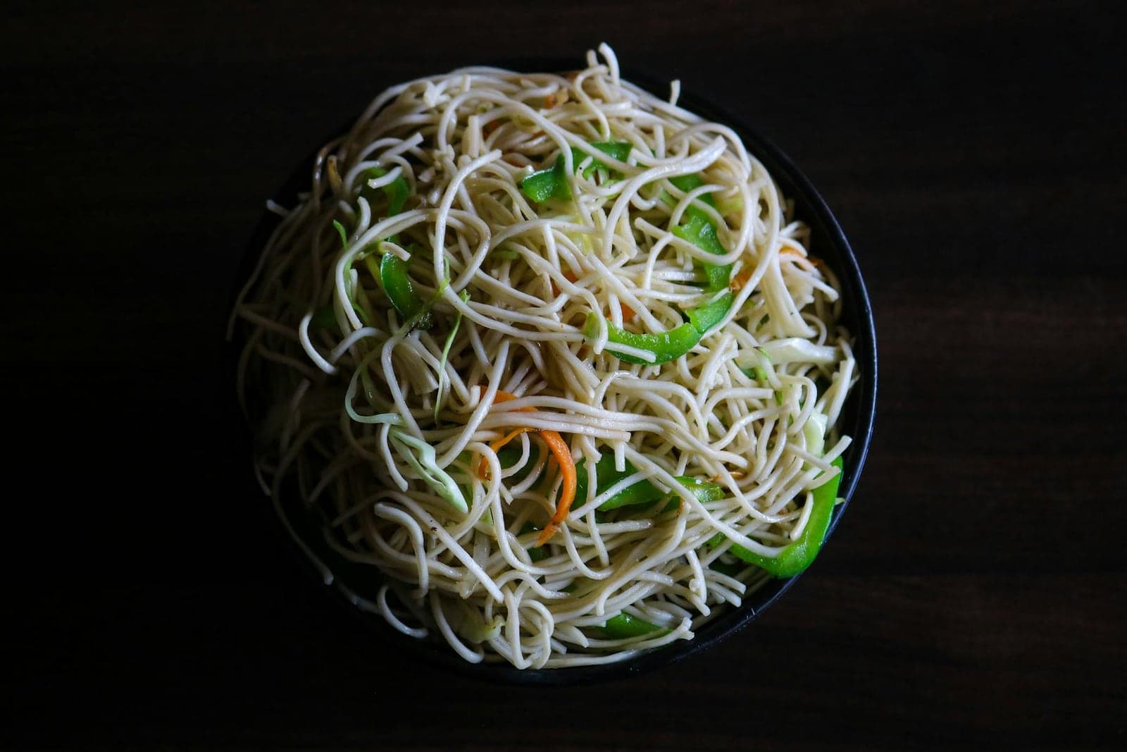 Hakka noodles stir-fried with vegetables and served in a dark bowl