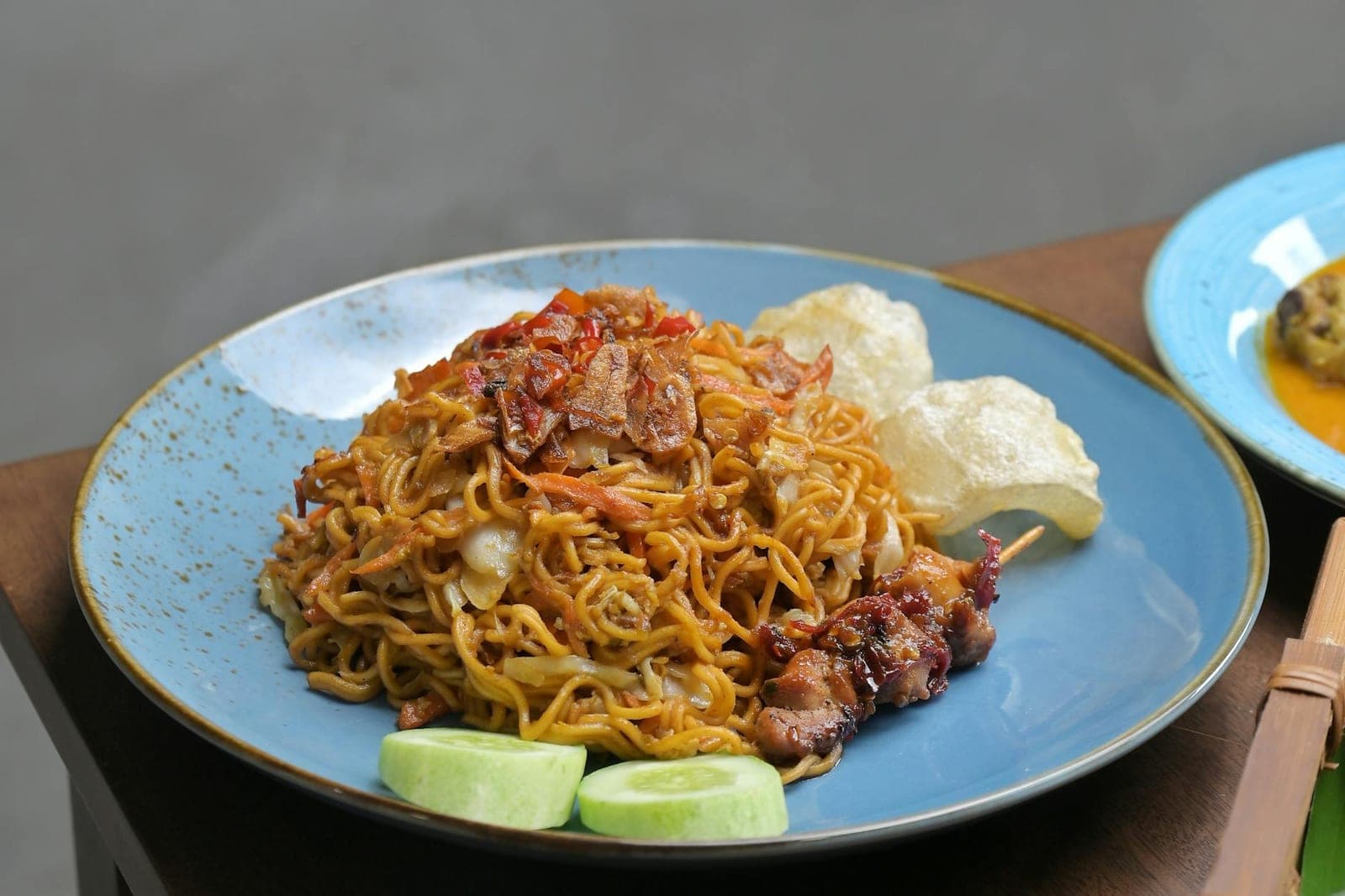 Indonesian mie goreng noodles with cucumber, lime, crackers, and savory sauce on a blue plate