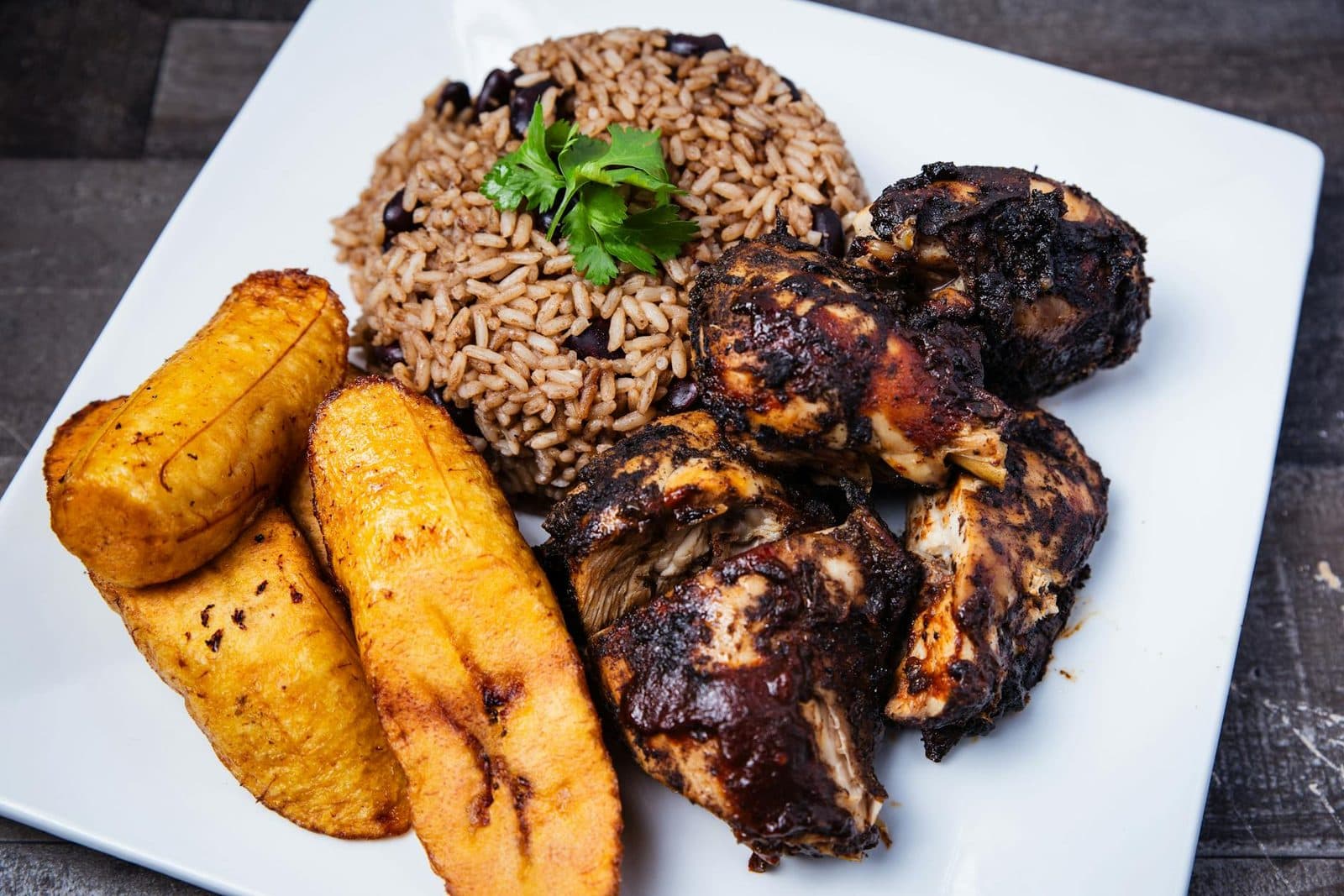 Jamaican jerk chicken with rice and beans and fried plantains on a square plate