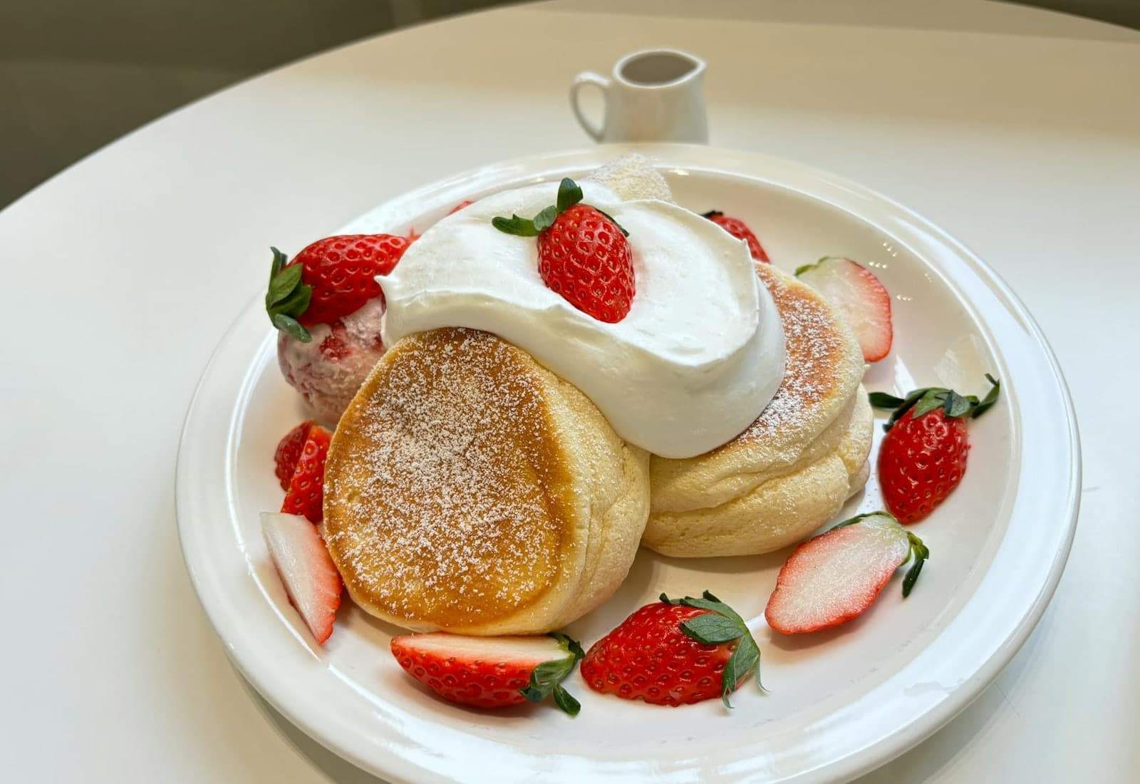 Japanese fluffy souffle pancakes topped with strawberries and cream on a white plate