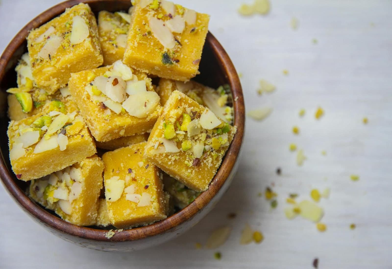 Kaju barfi Indian cashew-style sweets cut into squares with nuts and pistachios in a bowl