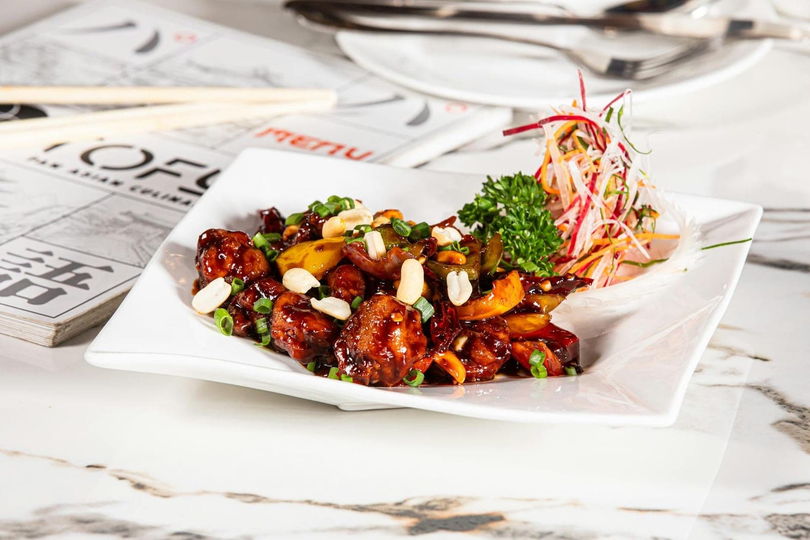 Kung Pao chicken with peanuts, chilies, scallions, and glossy sauce on a white plate