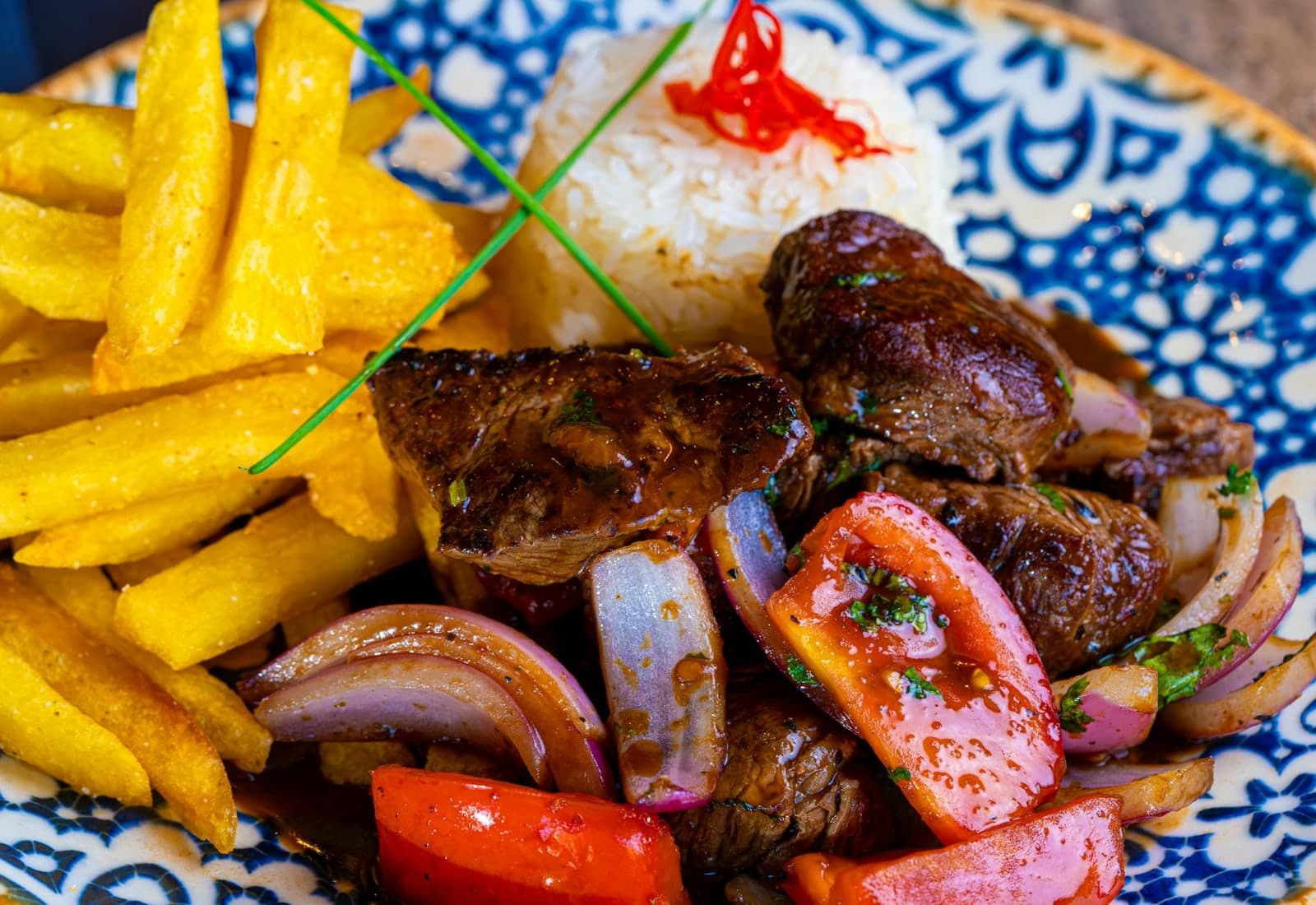 Lomo saltado with seared beef, fries, rice, onions, and tomatoes on a patterned plate
