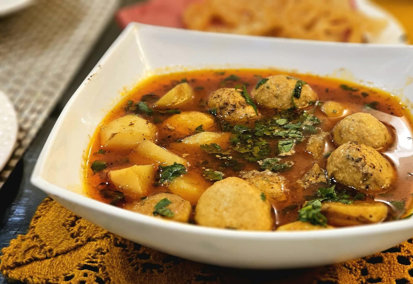 Malai kofta-style curry with round kofta pieces, potatoes, herbs, and warm sauce