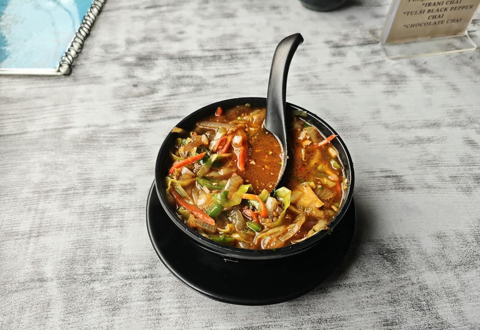 Manchow soup-style vegetable soup with noodles and vegetables in a black bowl