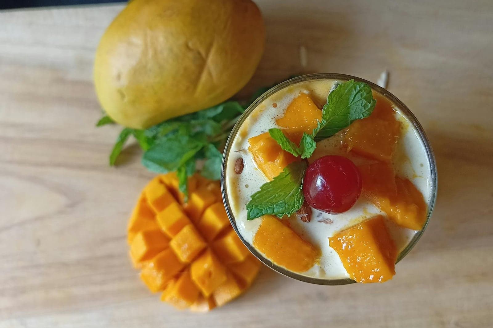 Mango lassi in a glass with mango pieces, mint, and a cherry garnish