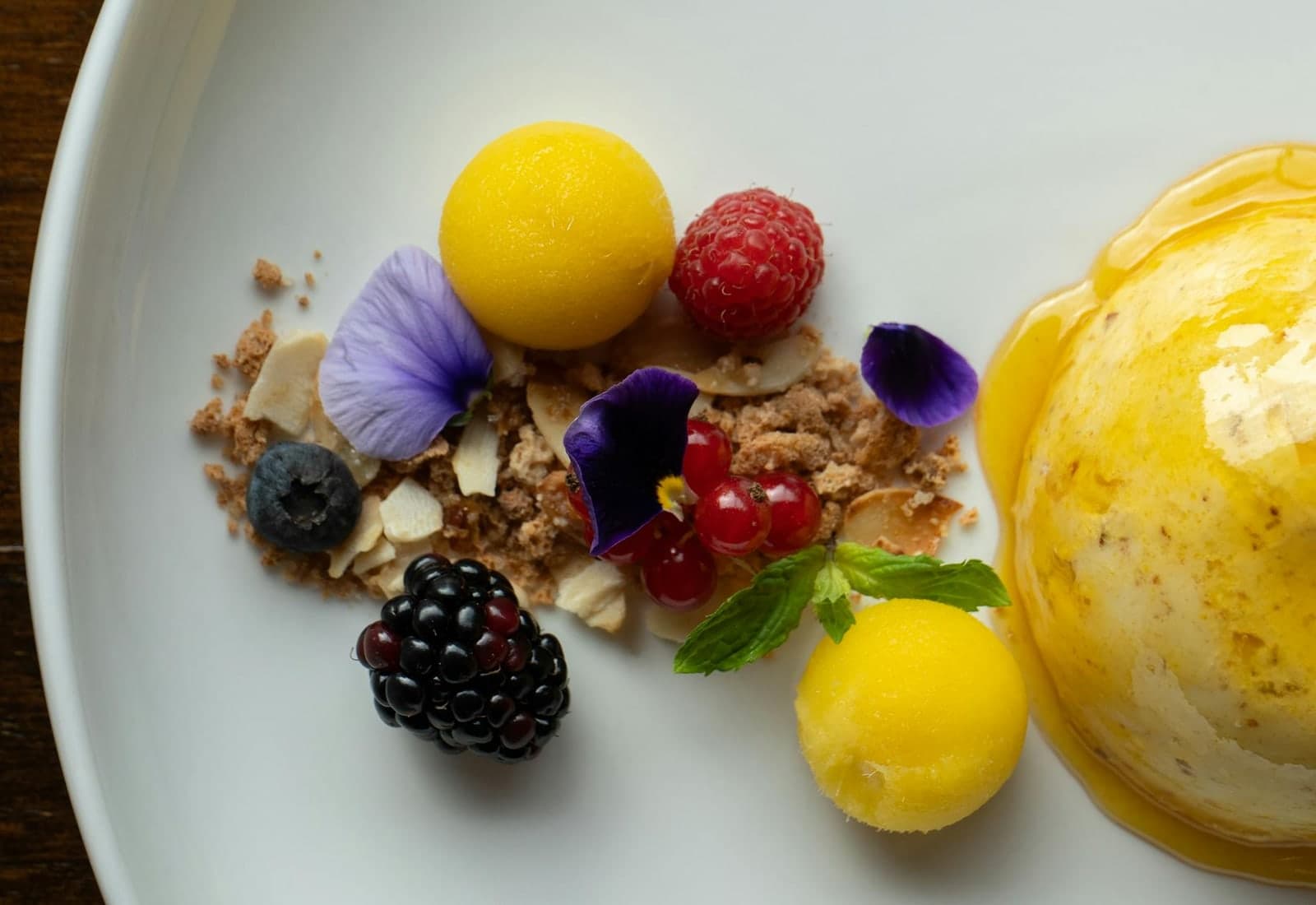 Mango sorbet dessert with bright yellow scoops, berries, and edible flowers on a plate