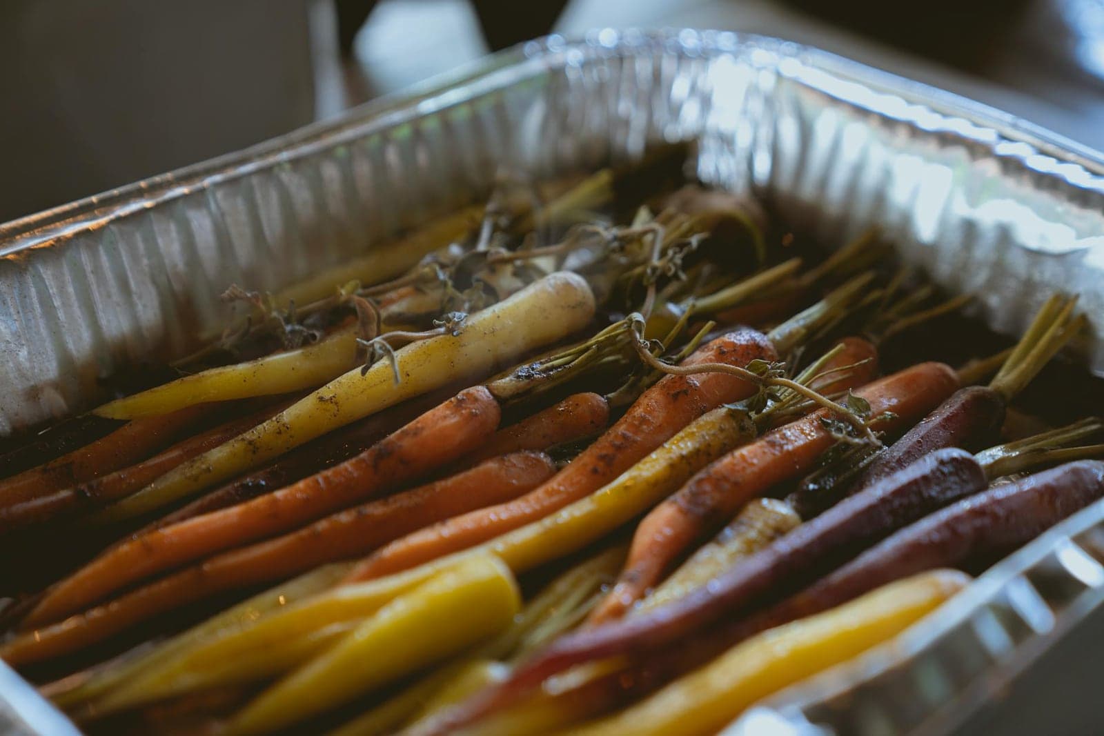 Maple roasted rainbow carrots with herbs in a foil roasting pan