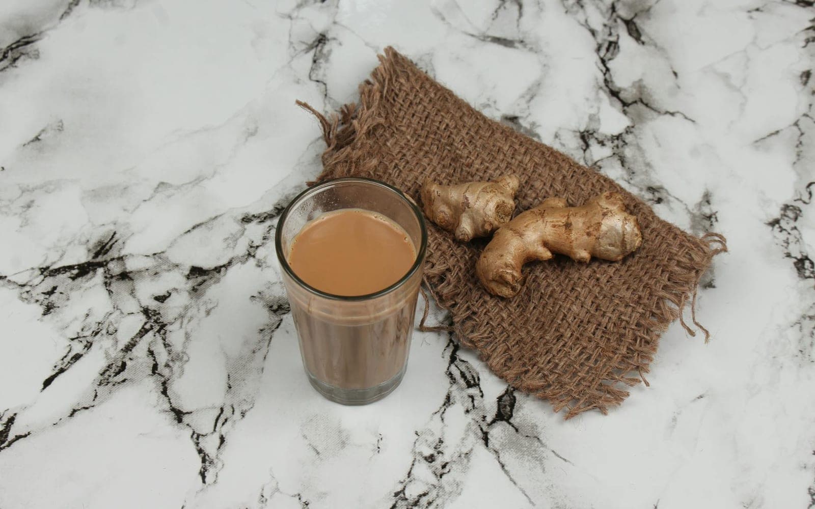 Masala chai in a glass with ginger on a marble surface