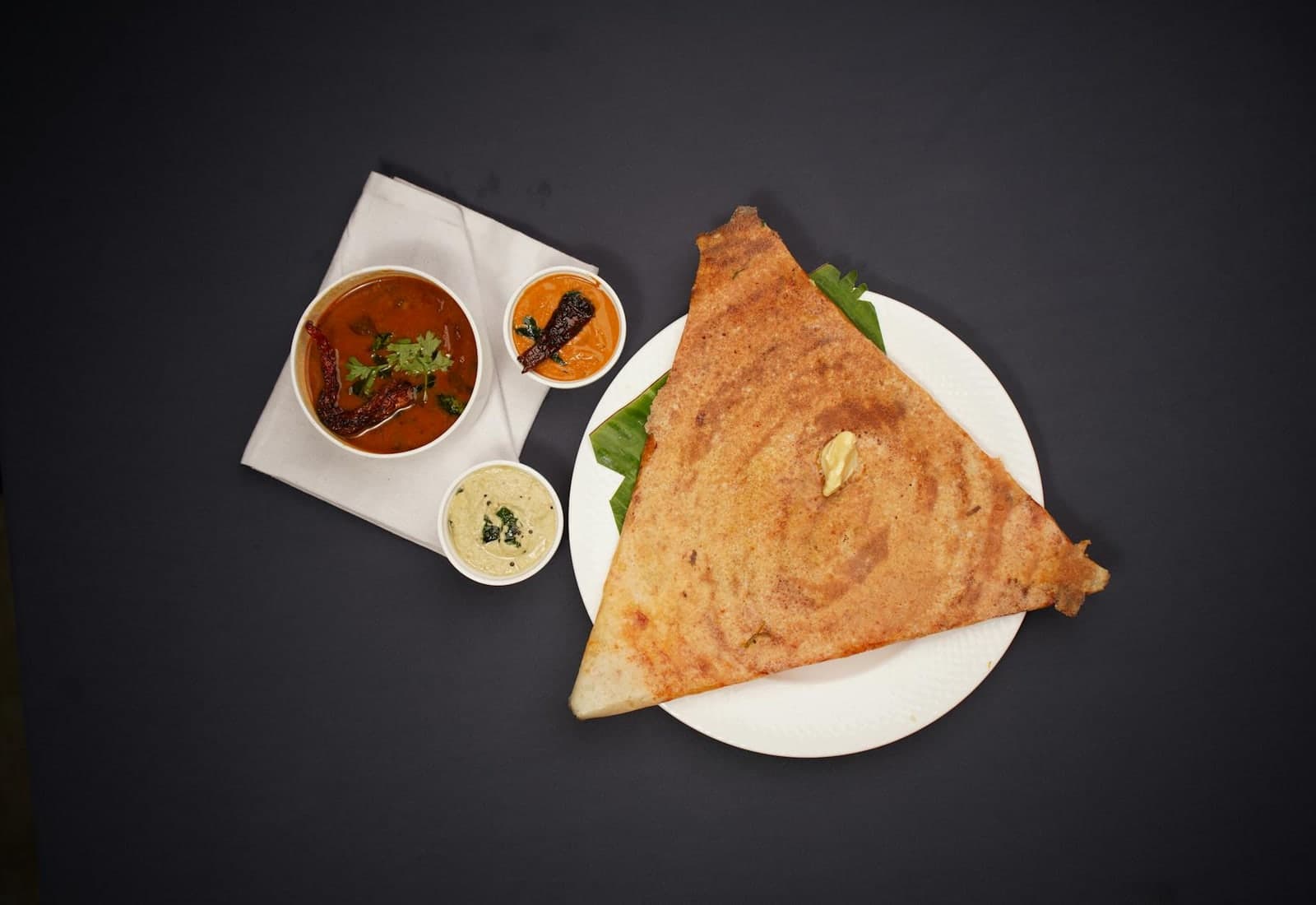 Masala dosa served with chutneys and sambar on a dark background