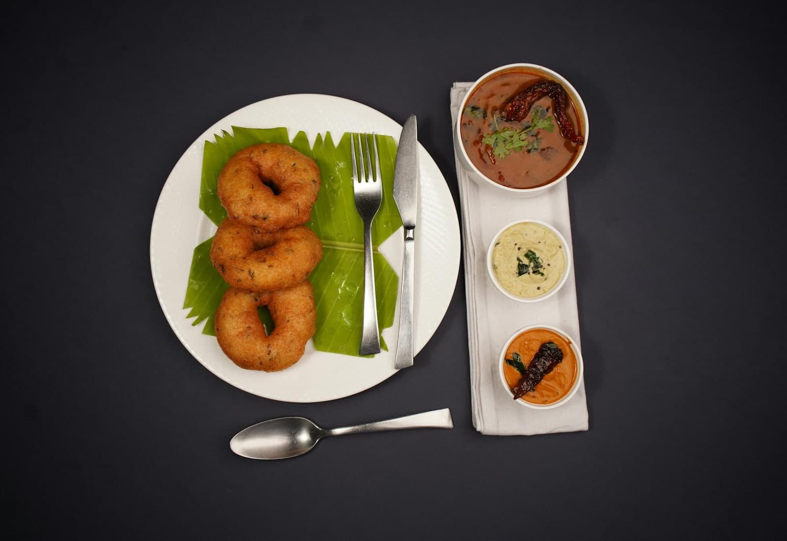 Medu vada South Indian fried lentil doughnuts served with chutneys and sambar on a black background