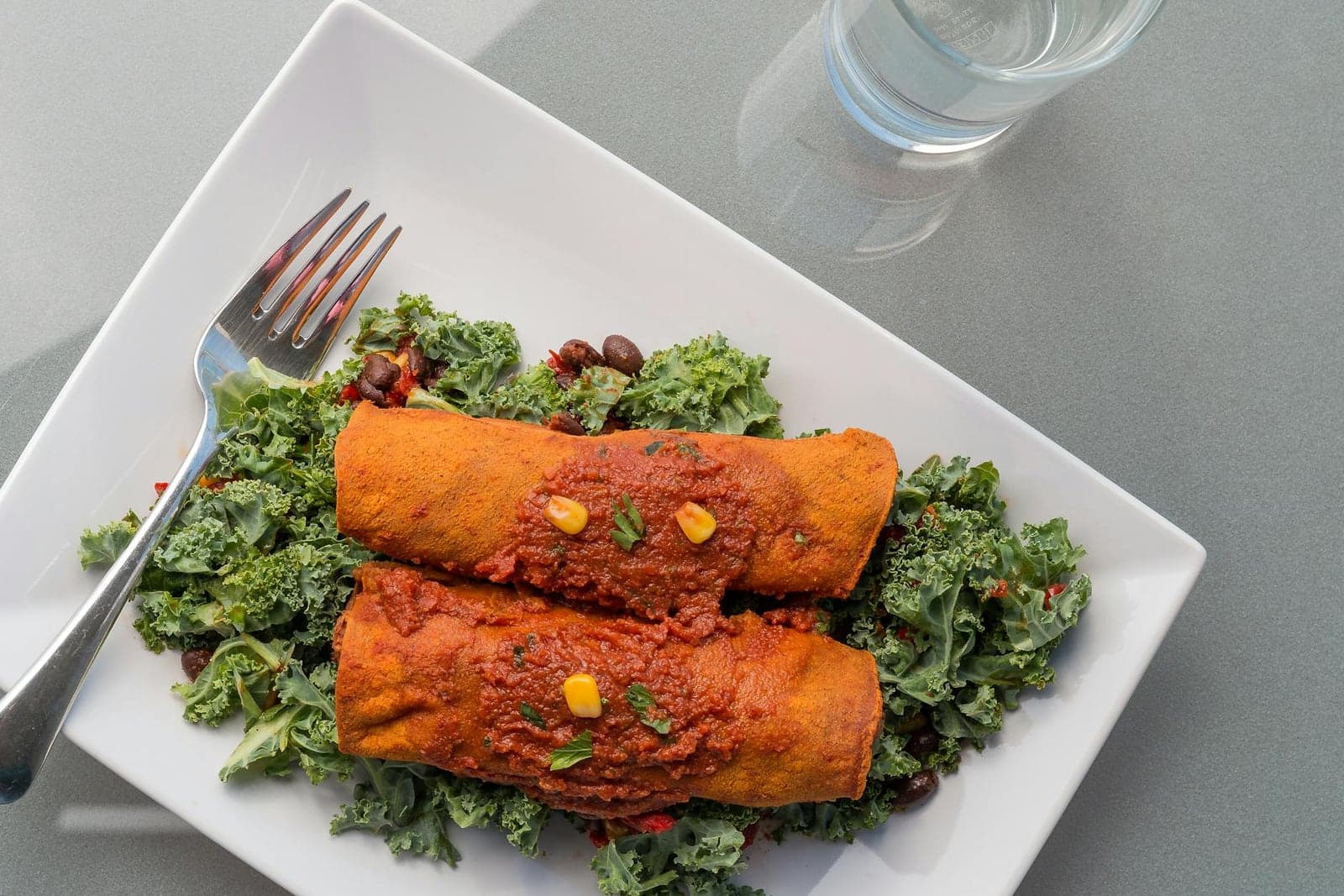 Mexican black bean enchiladas with red sauce, greens, and a fork on a plate