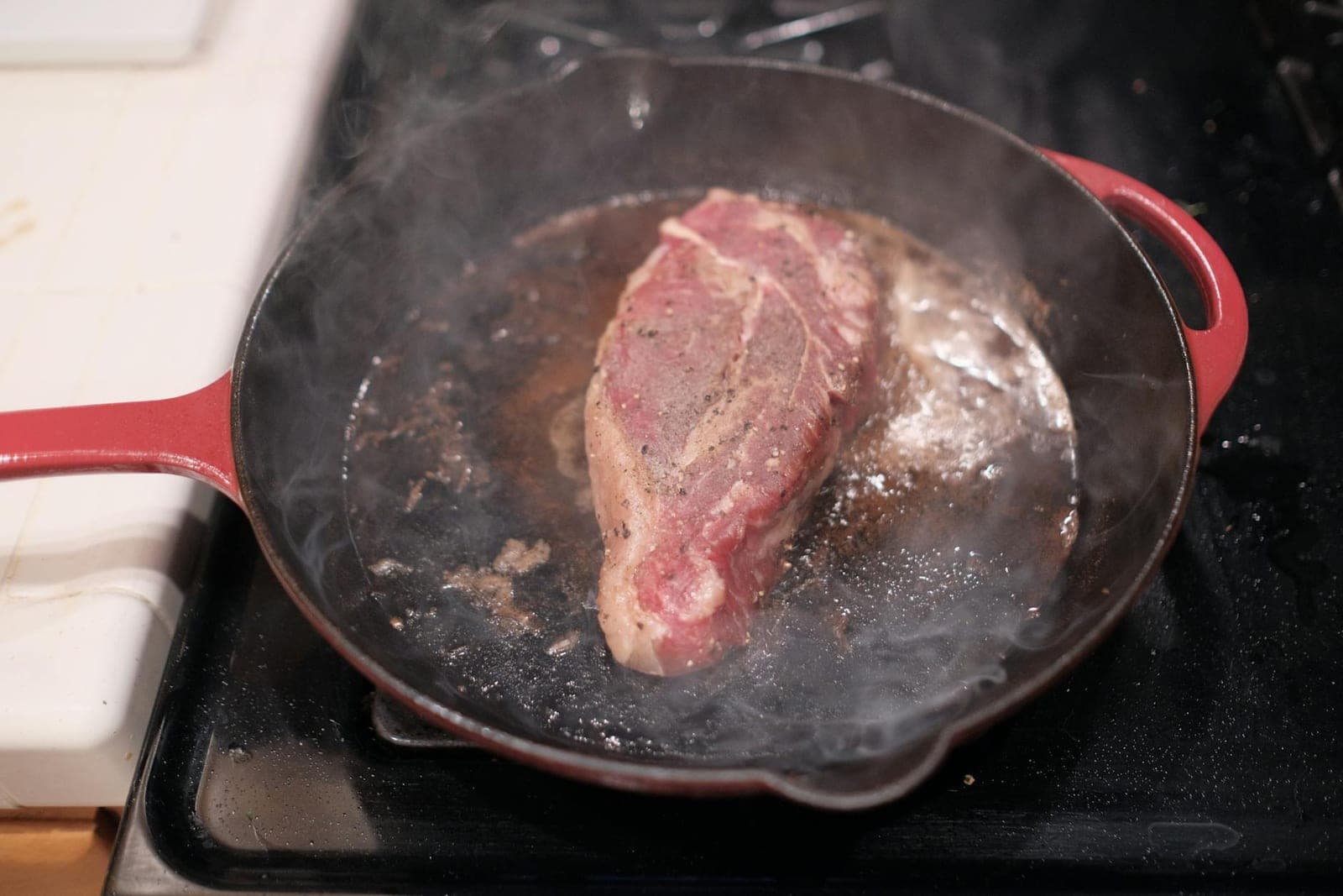 NY strip steak searing in a cast iron skillet with steam rising from the pan