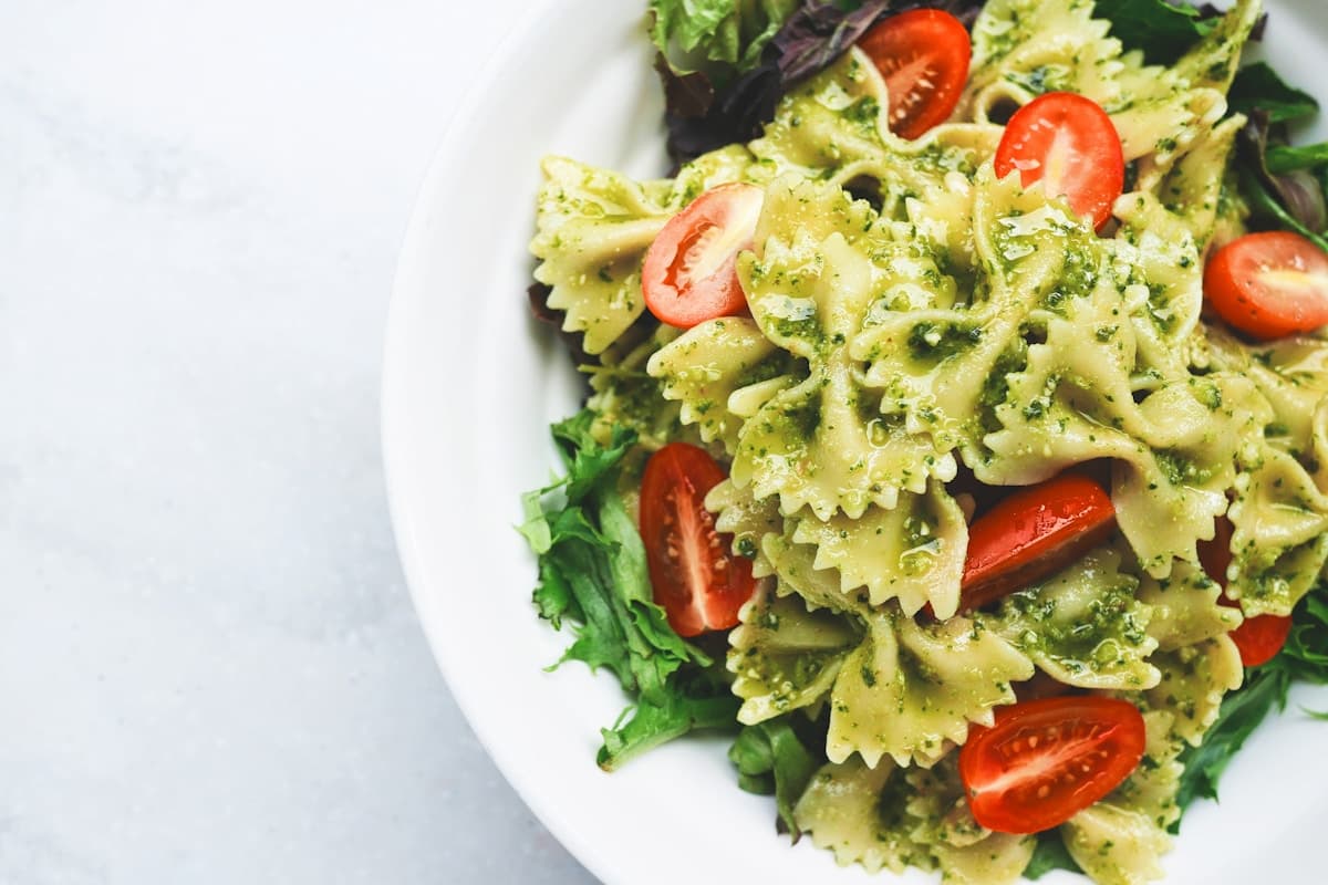 Pesto pasta primavera with colorful vegetables in a large white serving bowl
