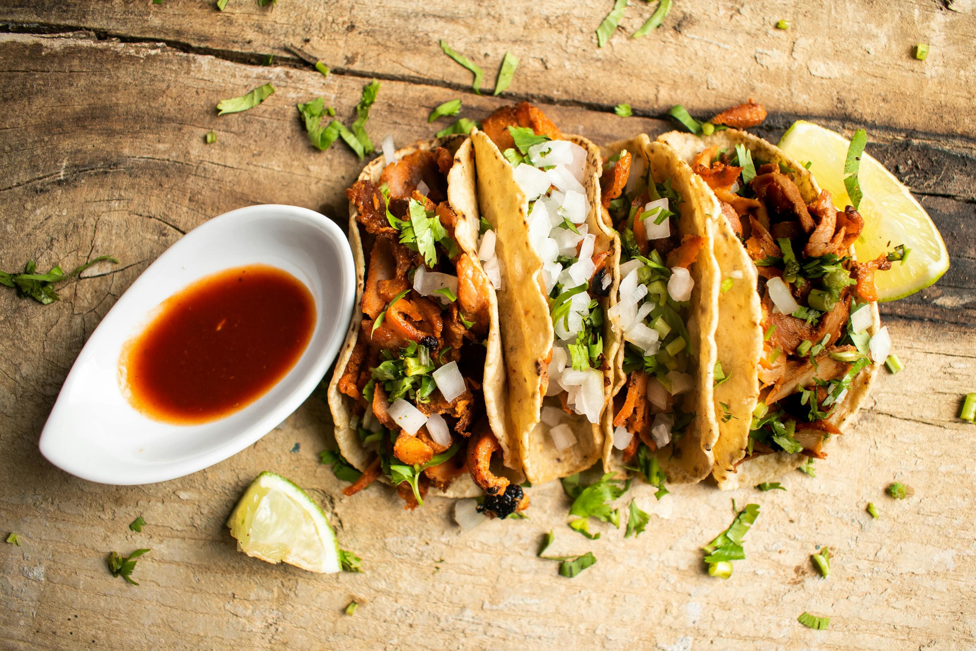Pork al pastor tacos with cilantro, onion, lime, and salsa on a rustic table