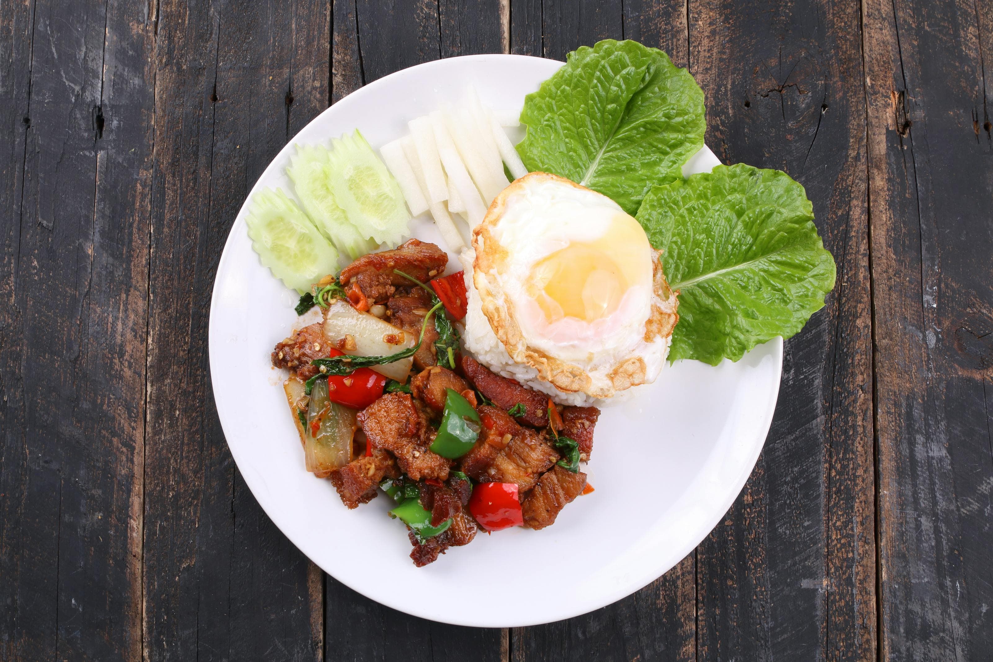 Pork fried rice with egg, vegetables, and crisp greens served on a white plate