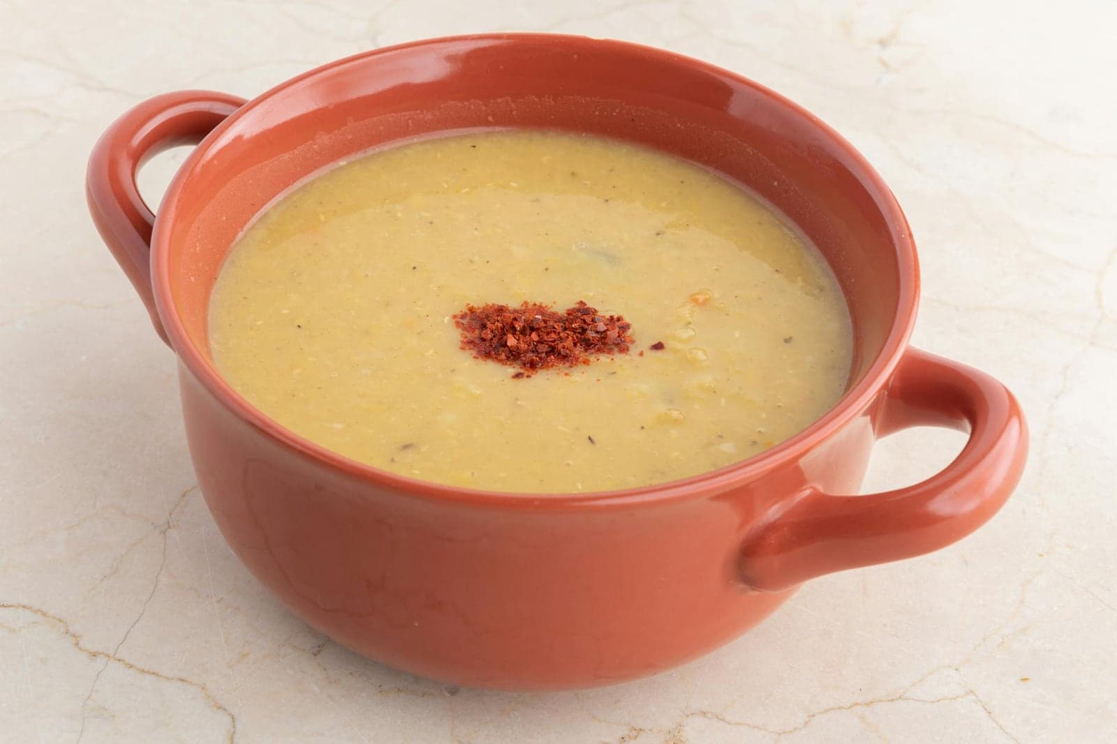 Red lentil soup in a terracotta handled bowl with paprika garnish