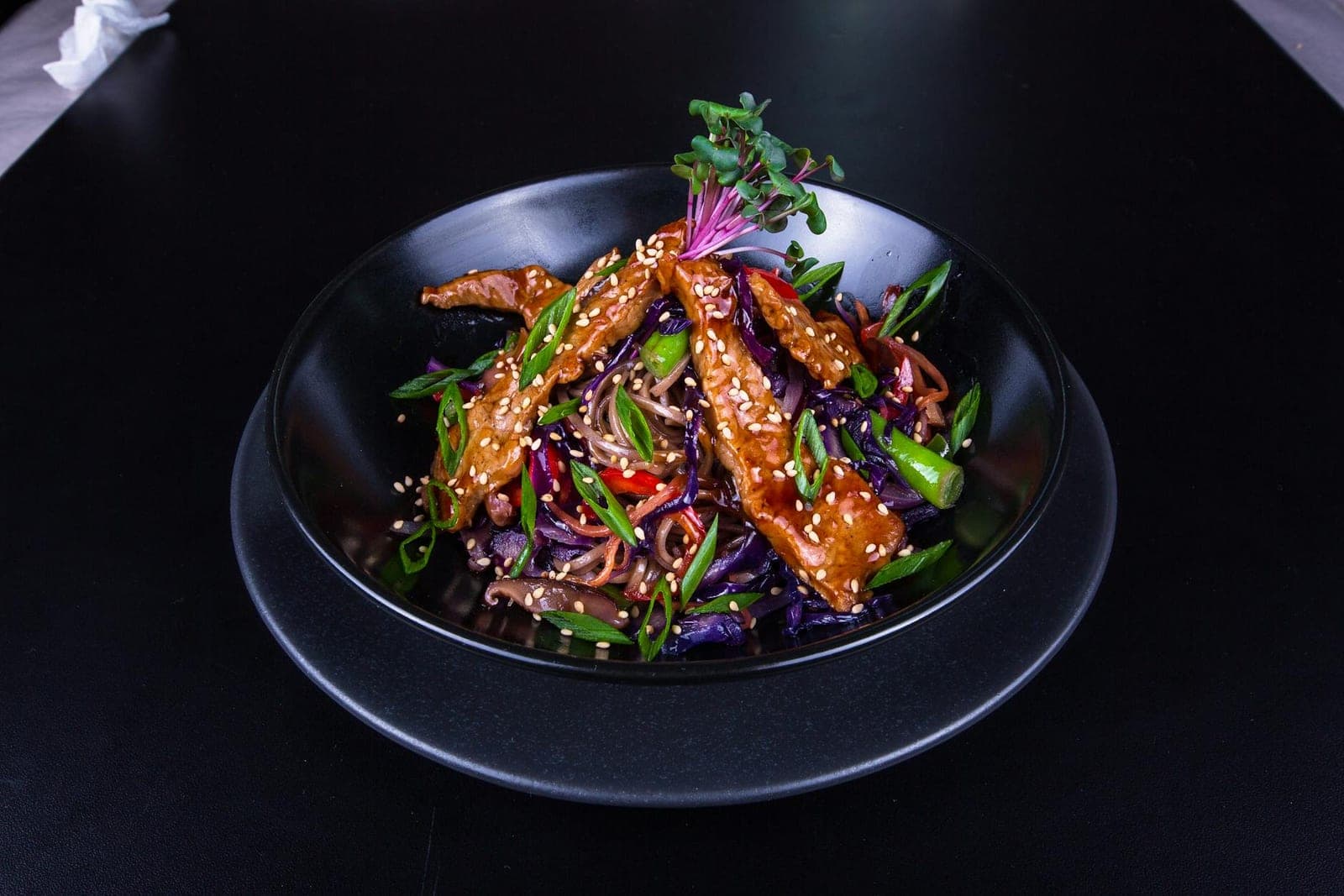Sesame ginger chicken stir-fry with vegetables and noodles in a black bowl