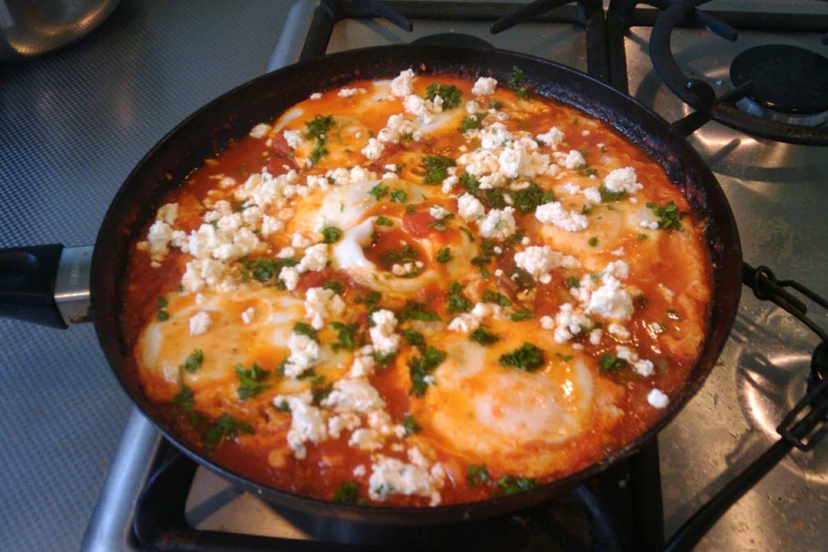 Shakshuka in a skillet with eggs poached in spiced tomato sauce and herbs