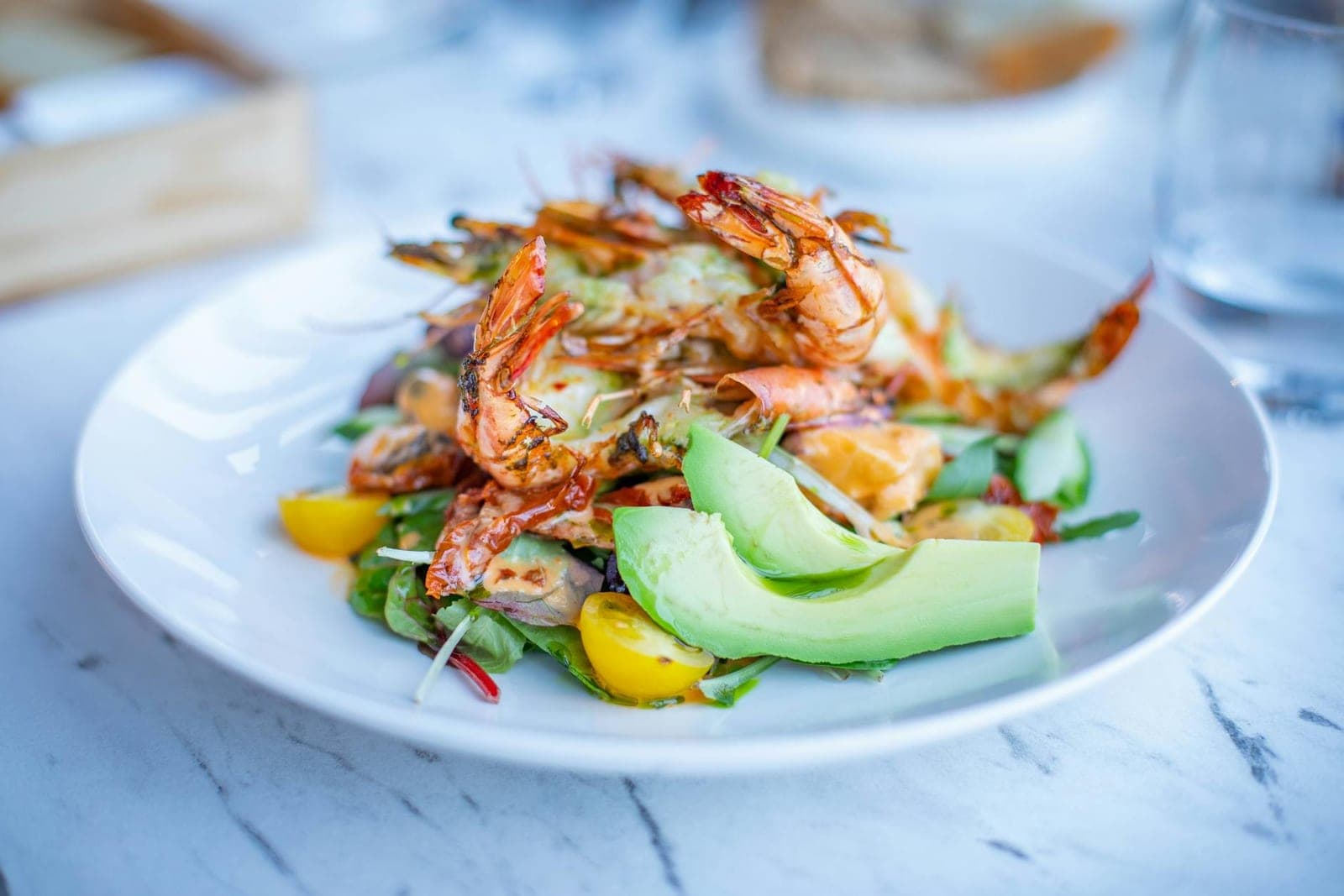 Shrimp avocado salad with greens, tomatoes, and creamy avocado on a white plate