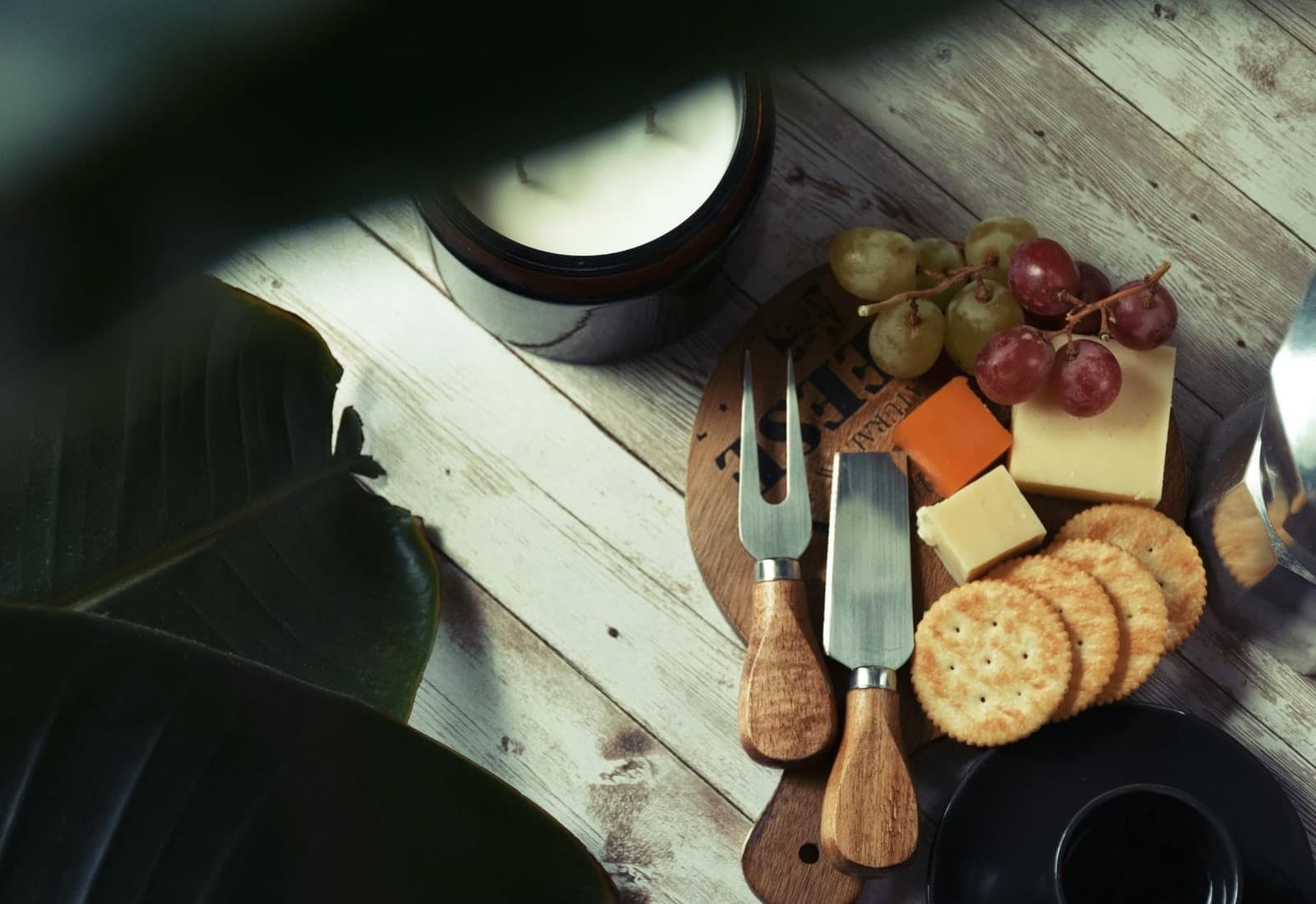 Simple cheese board with cheese, crackers, grapes, and cutlery on a rustic wooden board