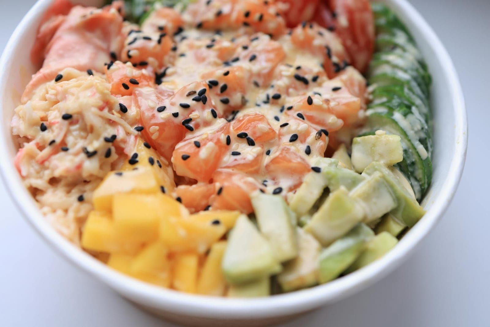 Spicy salmon poke bowl with avocado, mango, rice, sesame, and creamy sauce
