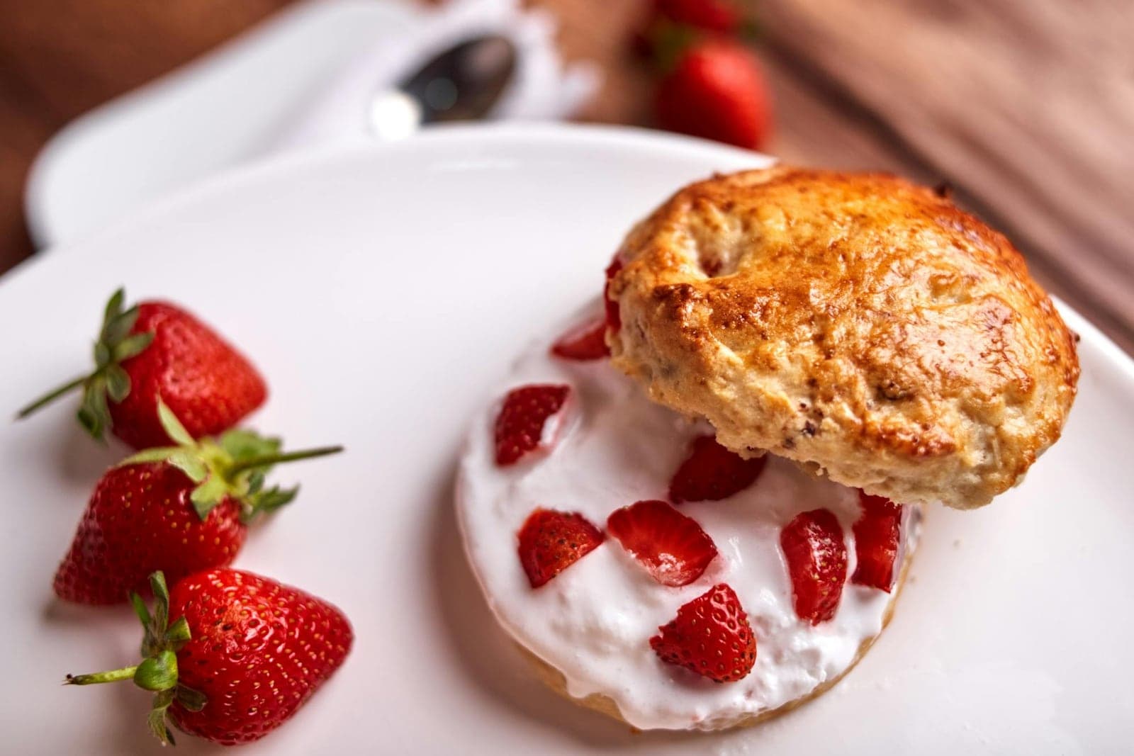 Strawberry shortcake with whipped cream, fresh strawberries, and split biscuits on a white plate