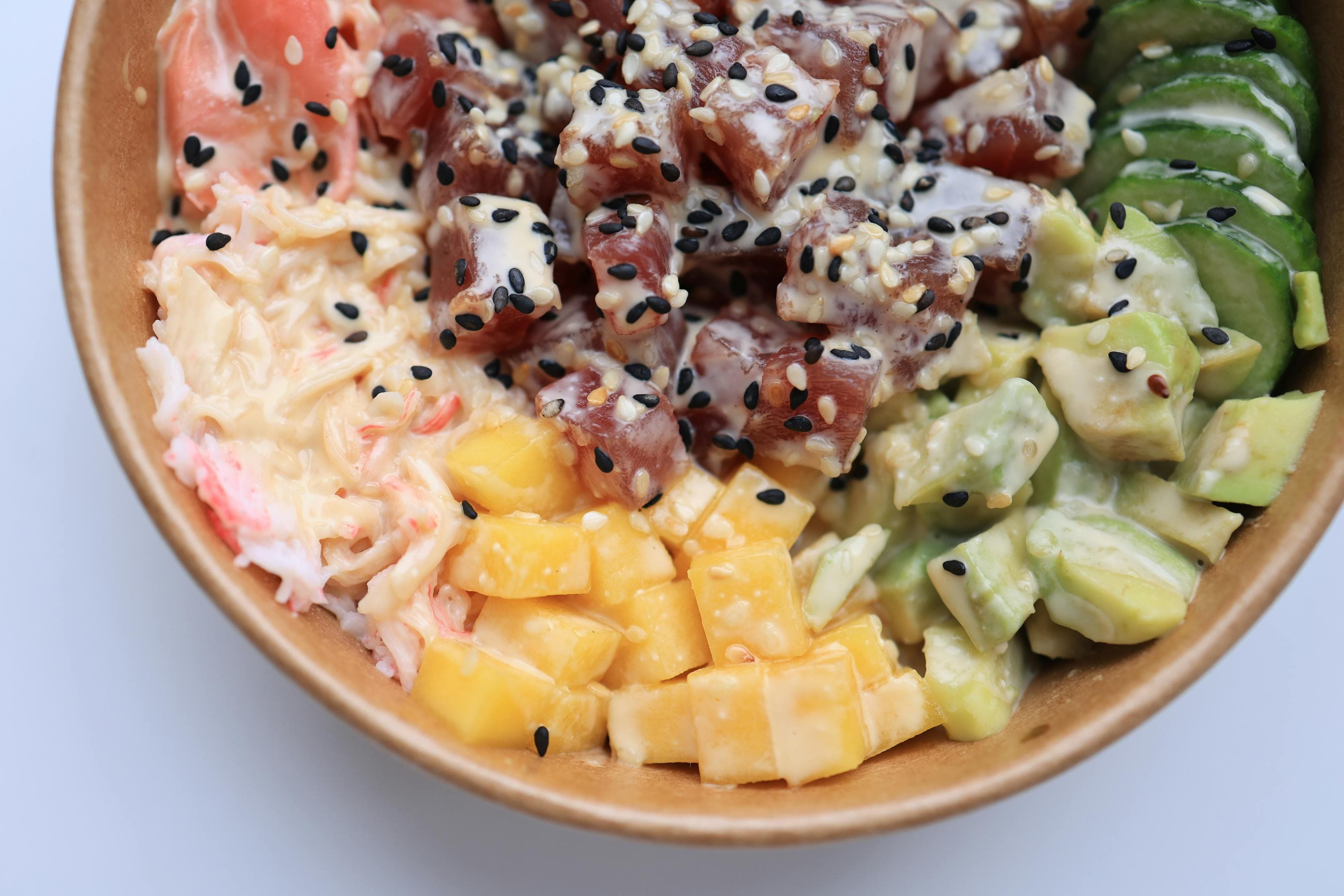 Tuna poke bowl with avocado, cucumber, mango, rice, sesame, and creamy sauce