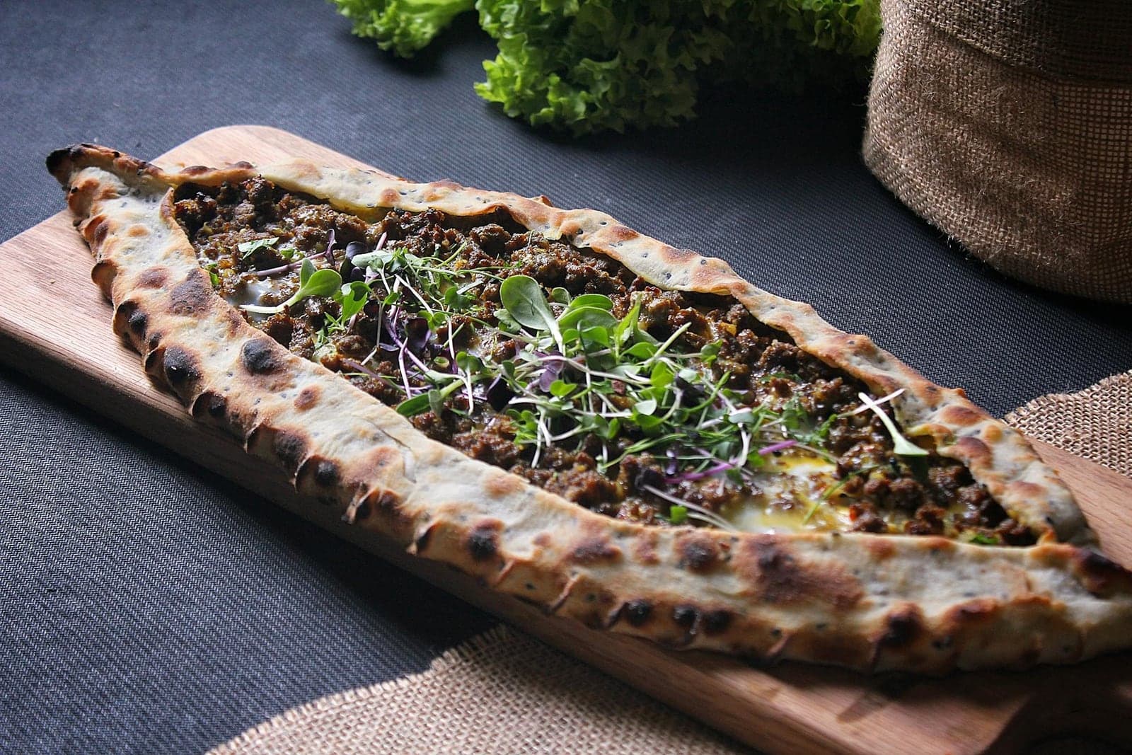 Turkish pide with minced meat filling and herbs on a wooden board
