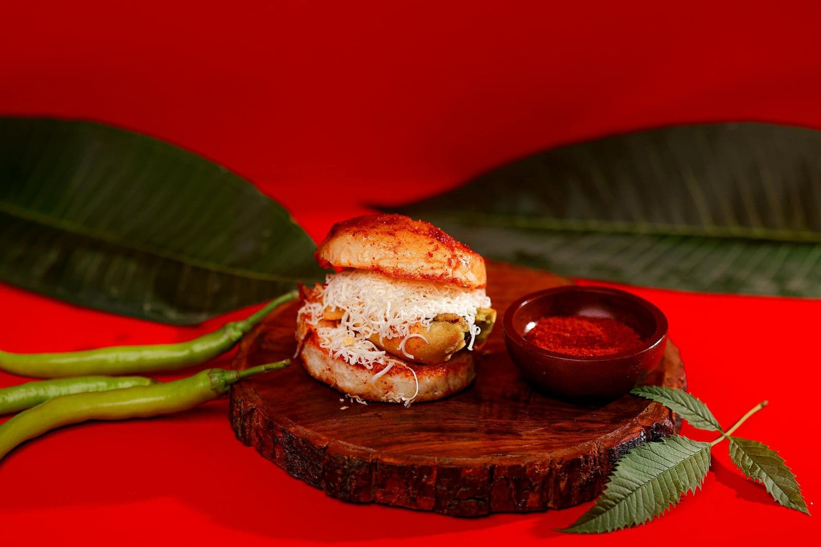 Vada pav served with green chilies and spicy chutney on a wooden plate