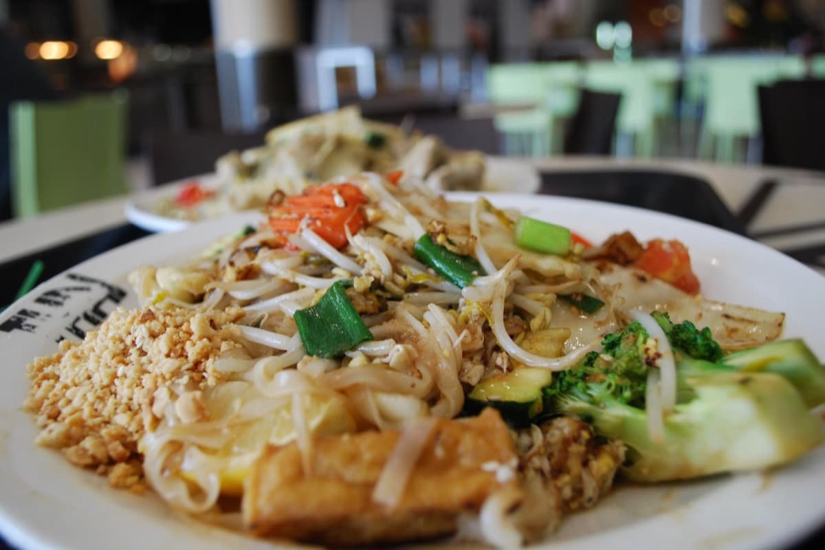 Plate of vegetable pad Thai with rice noodles, tofu, bean sprouts, peanuts, and lime wedges