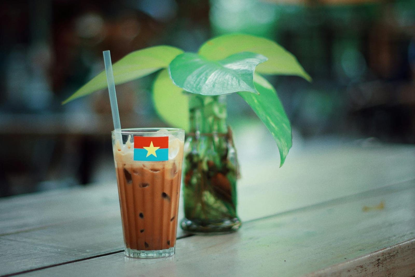 Vietnamese iced coffee in a tall glass with a straw on a wooden cafe table